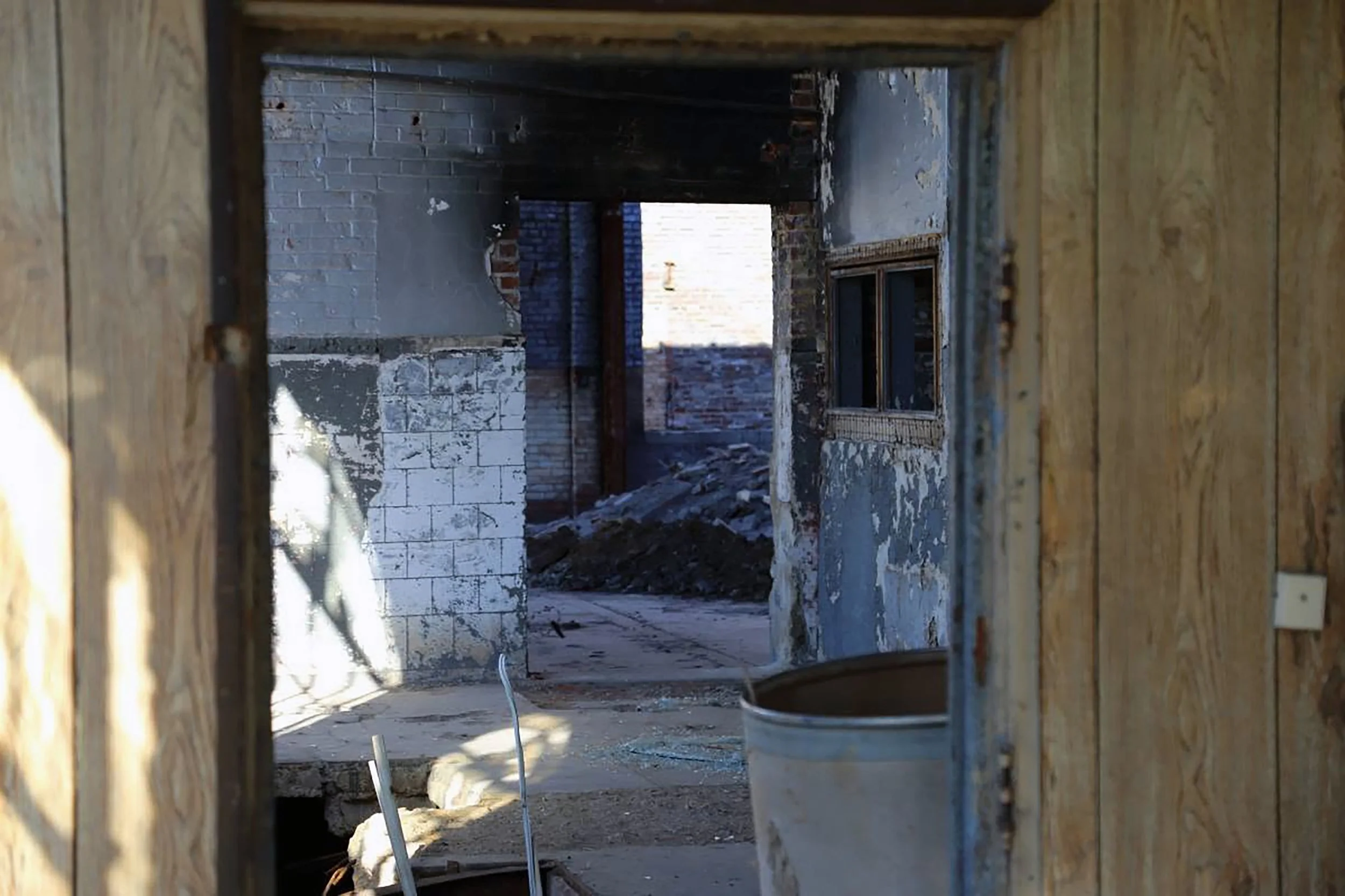 View through a small opening in a wooden wall of a construction site showing brick walls, concrete, and building materials inside.