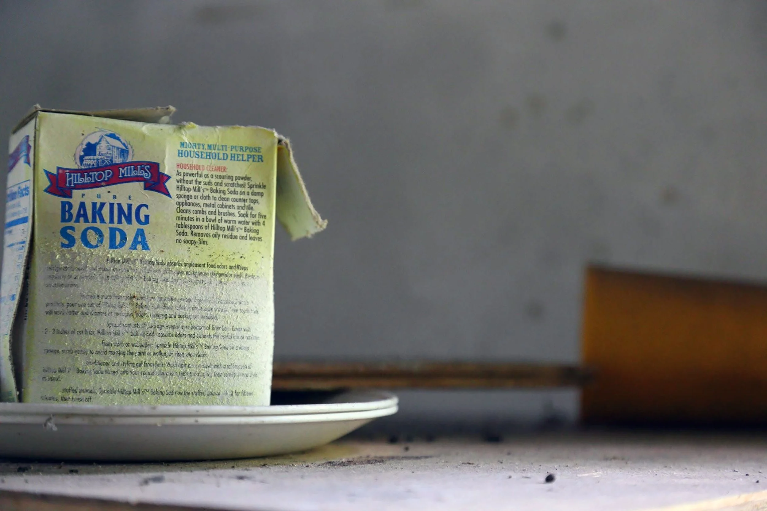 A partially torn box of Hilltop Mills Pure Baking Soda on a white plate with a gray wall background.