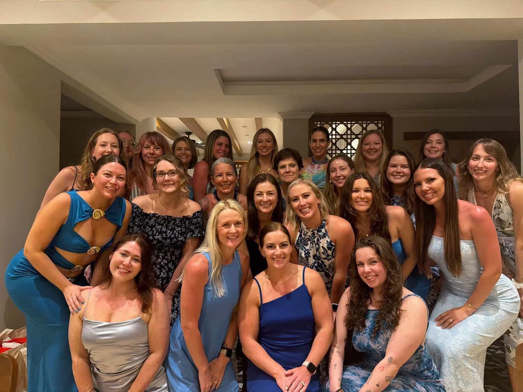 Group of women smiling and posing for a photo indoors, wearing colorful dresses and tops.