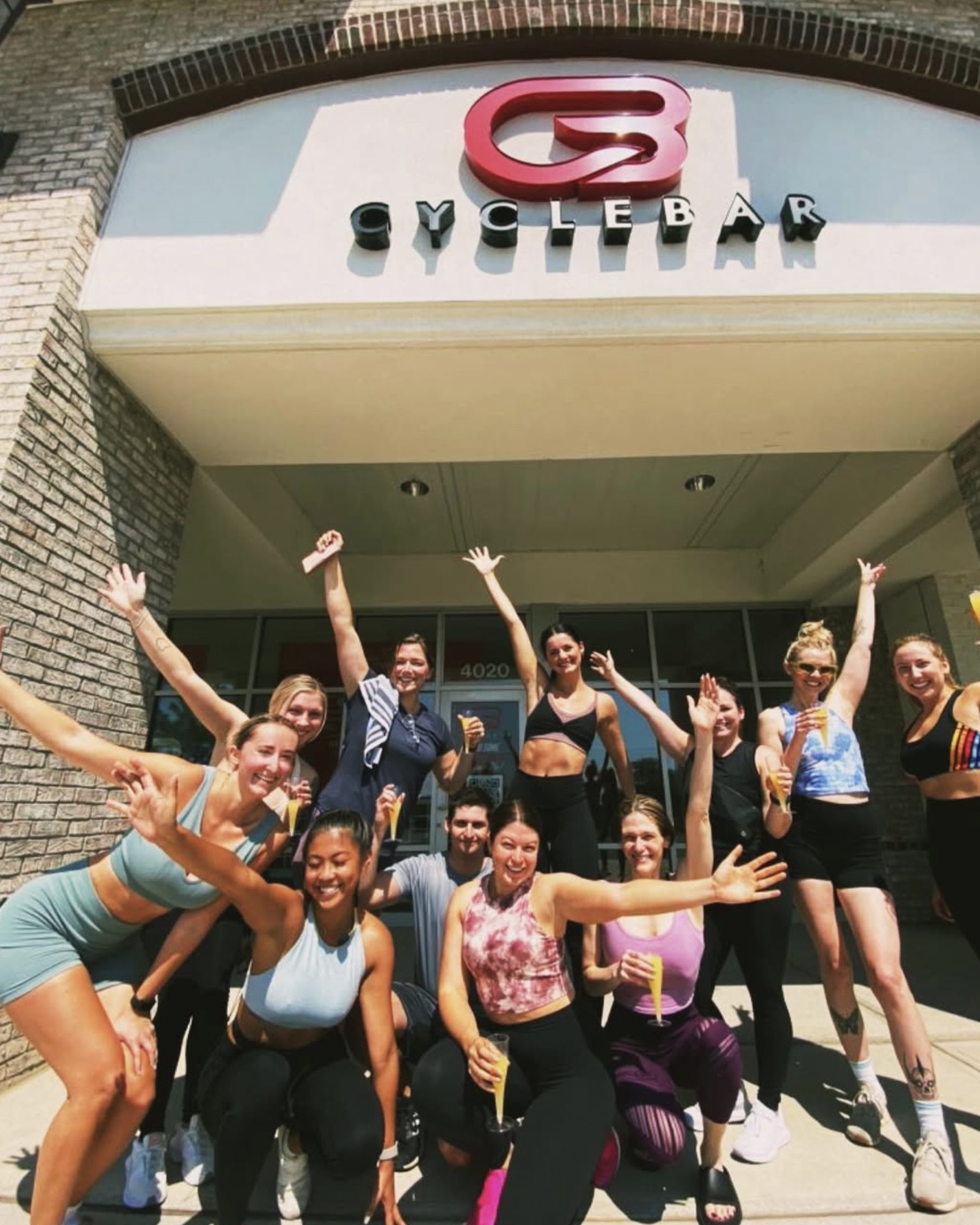 Group of people smiling and celebrating outside a building with a sign that reads 'Cyclebar' with a red logo above