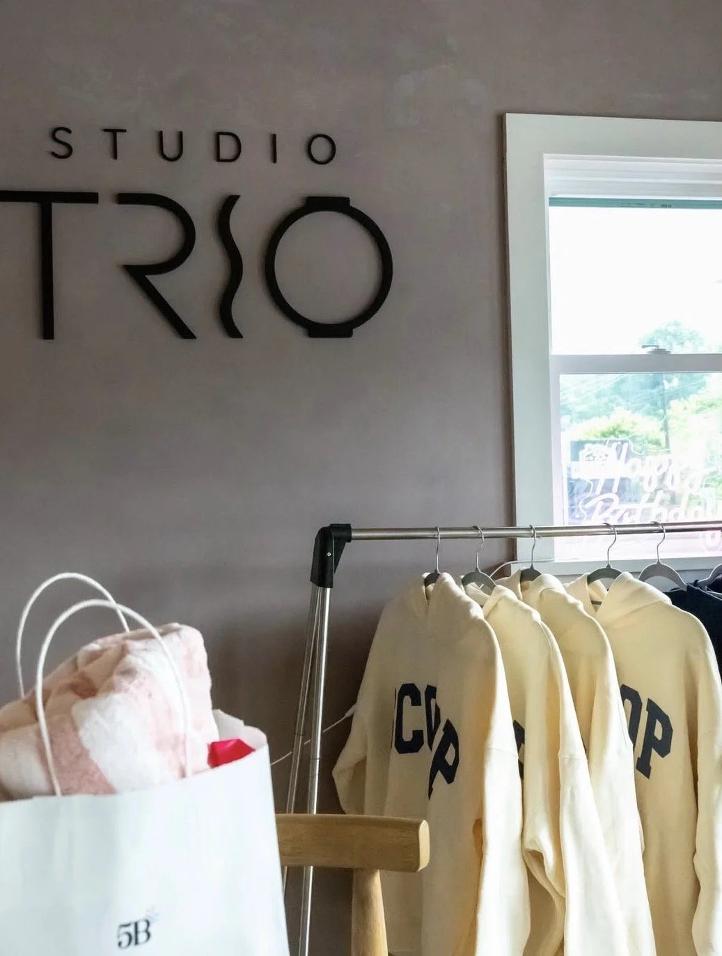 Interior of a clothing store with a sign that reads 'STUDIO TRIO', a window with a view outside, and a rack of yellow hoodies with the word 'CHOP' printed on them.