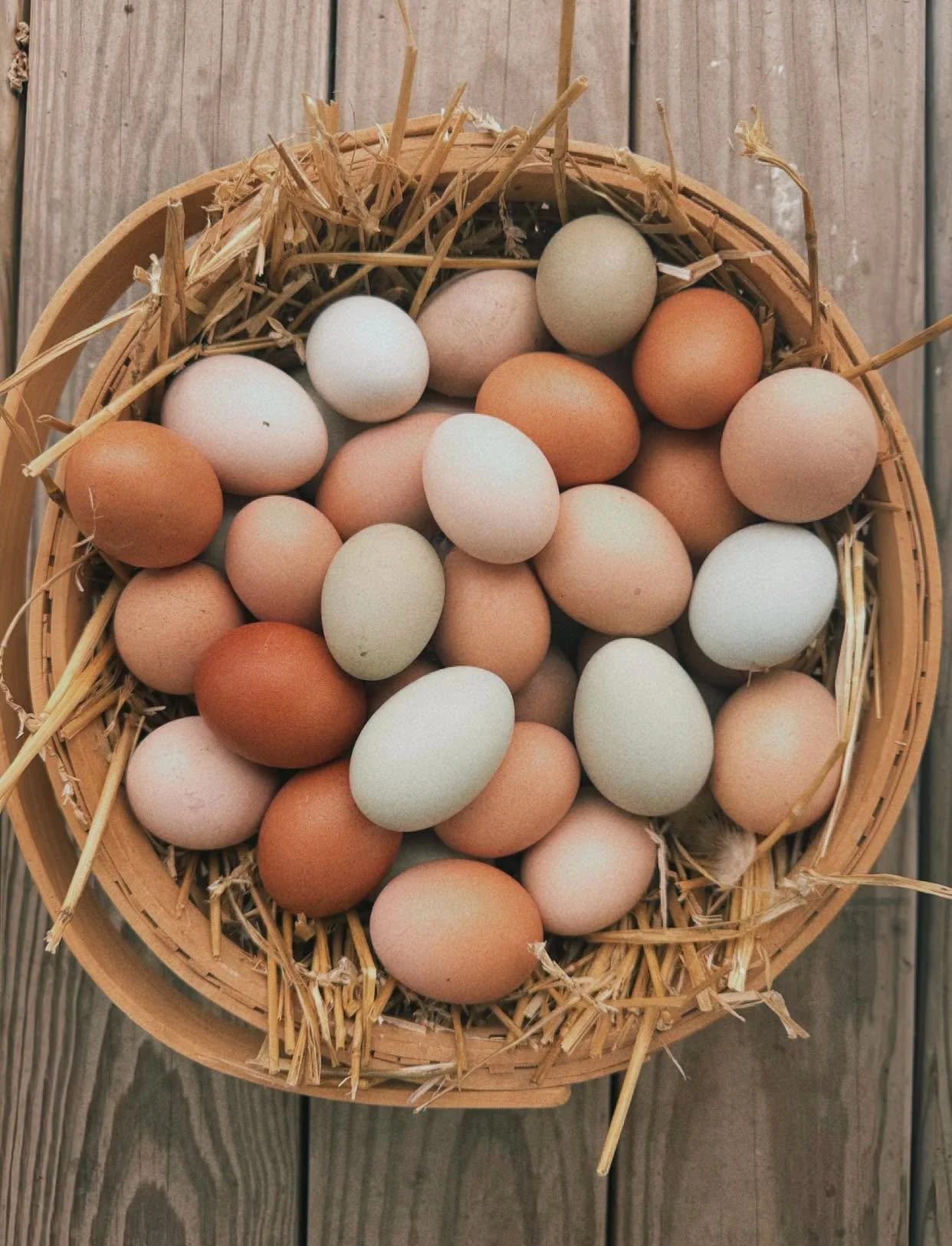 A wooden basket filled with various colored eggs resting on a wooden surface.