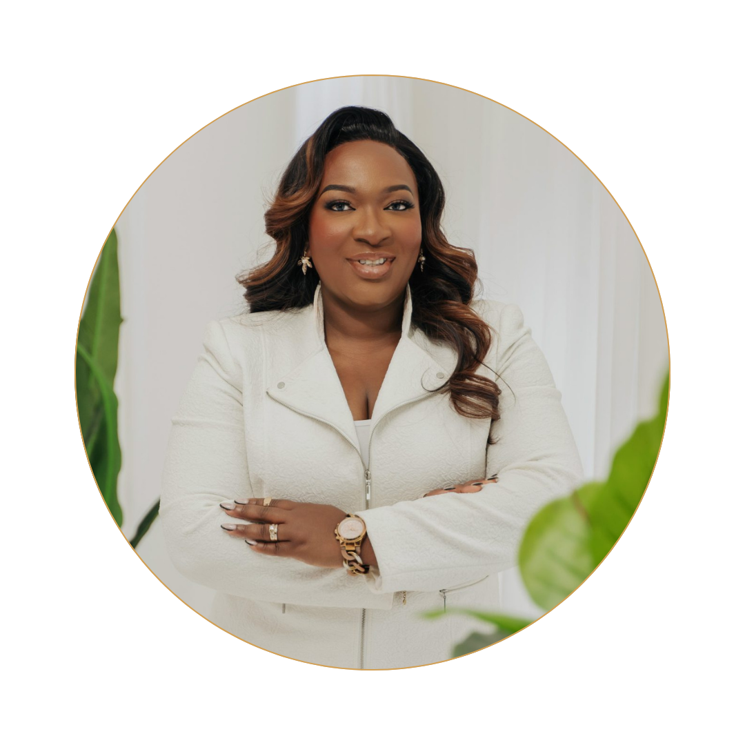 A confident woman with dark hair styled in loose waves, wearing a white textured blazer, gold jewelry, and smiling with arms crossed, indoors with white curtains and green plants in the background.