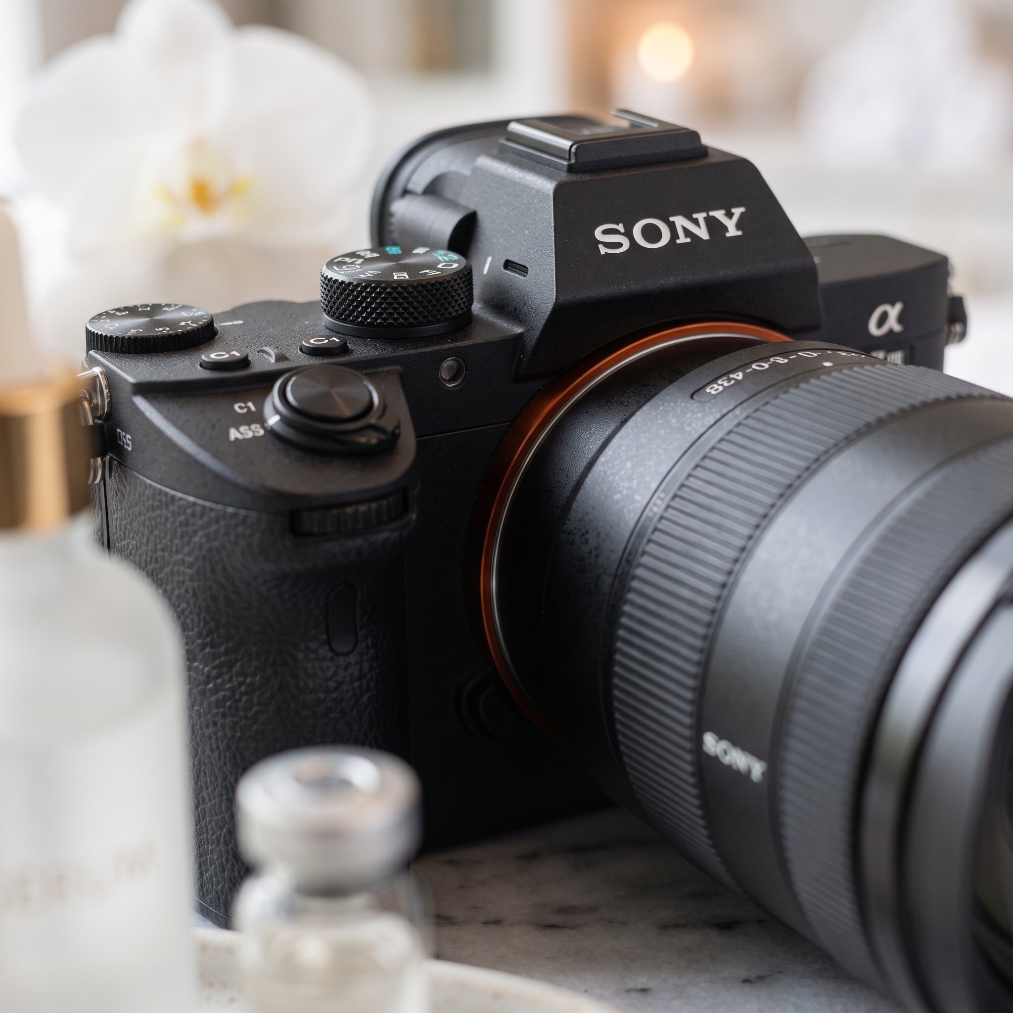 Close-up of a Sony camera with a zoom lens, taken from below, with blurred objects in the background.