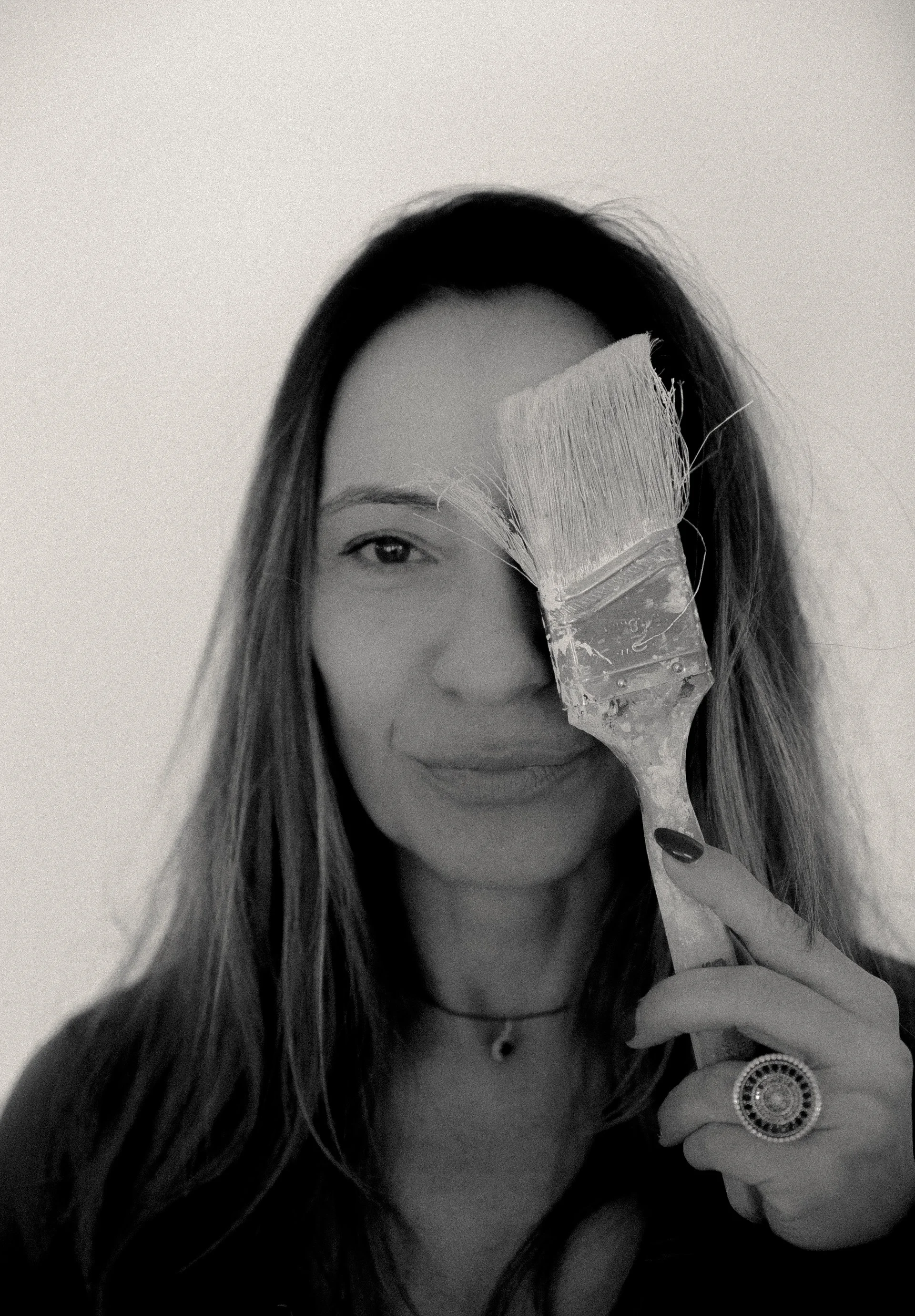 Black-and-white portrait of a woman holding a paintbrush over one eye