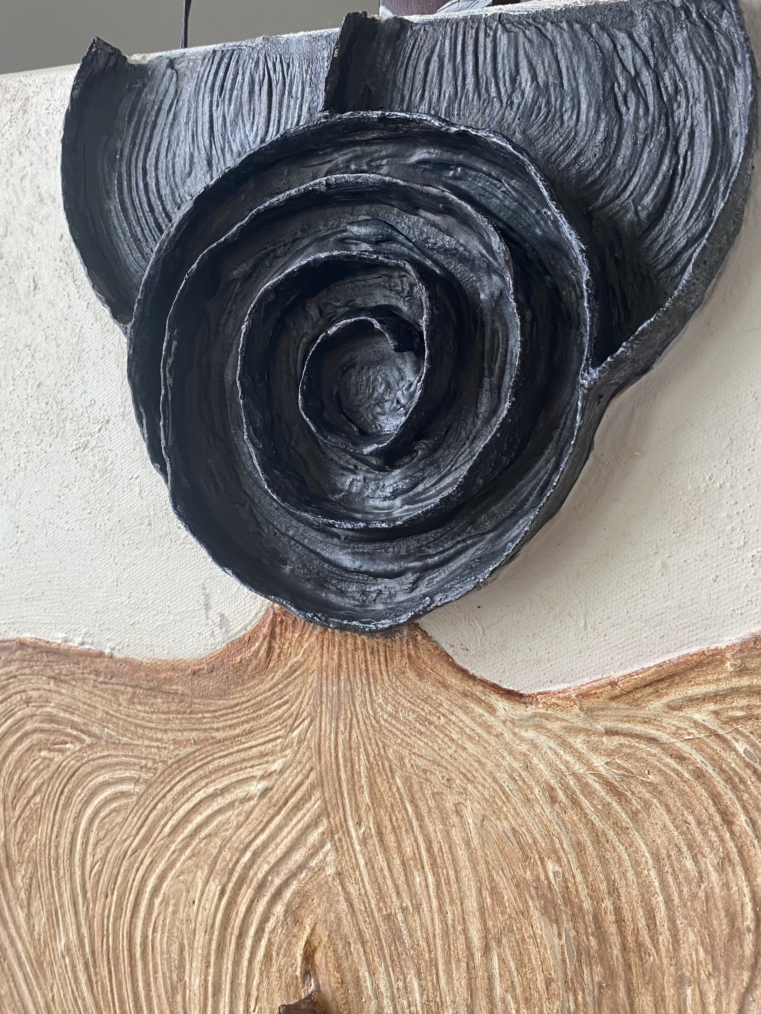 Close-up of a black carved wooden spiral sculpture mounted on a wall above a textured wood surface