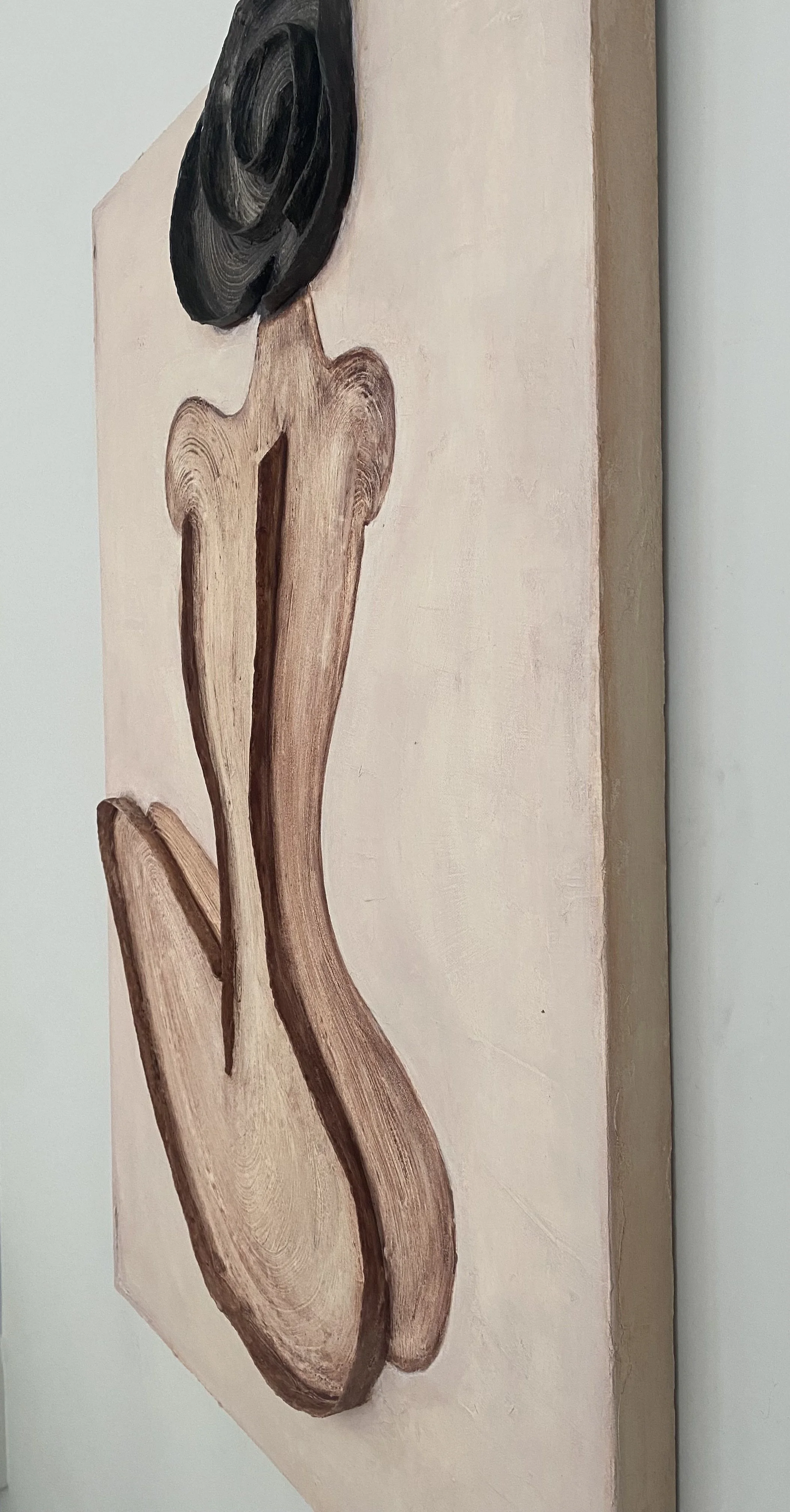 Close-up of a carved wooden sculpture with a black circular detail mounted on a pale wood panel