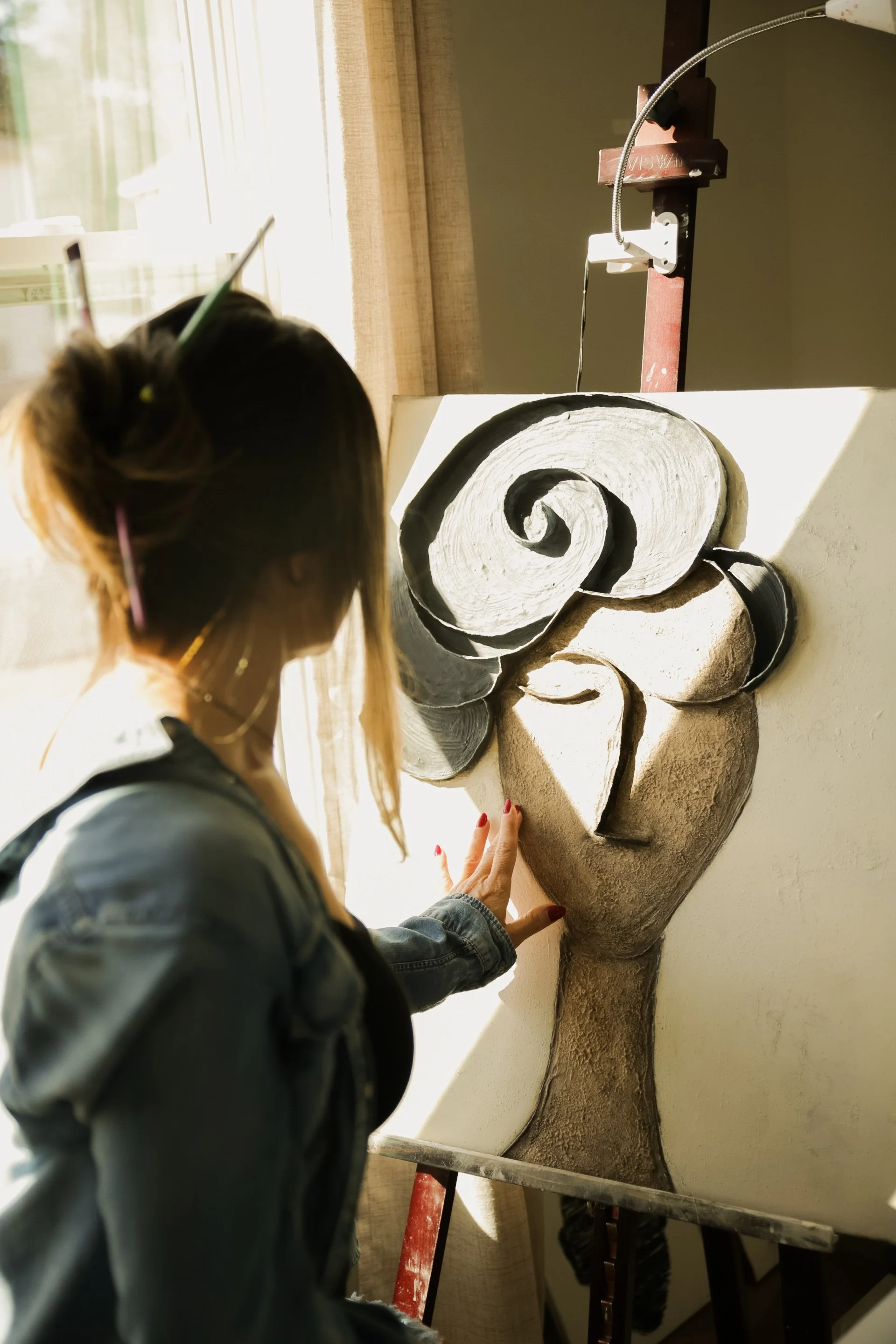 Artist working on a large sculpted human figure beside a sunlit window