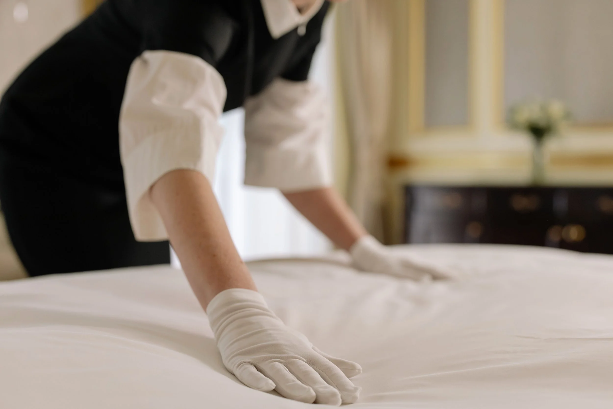 Behandschuhte Hand glättet sorgfältig die Bettwäsche eines Hotelbetts