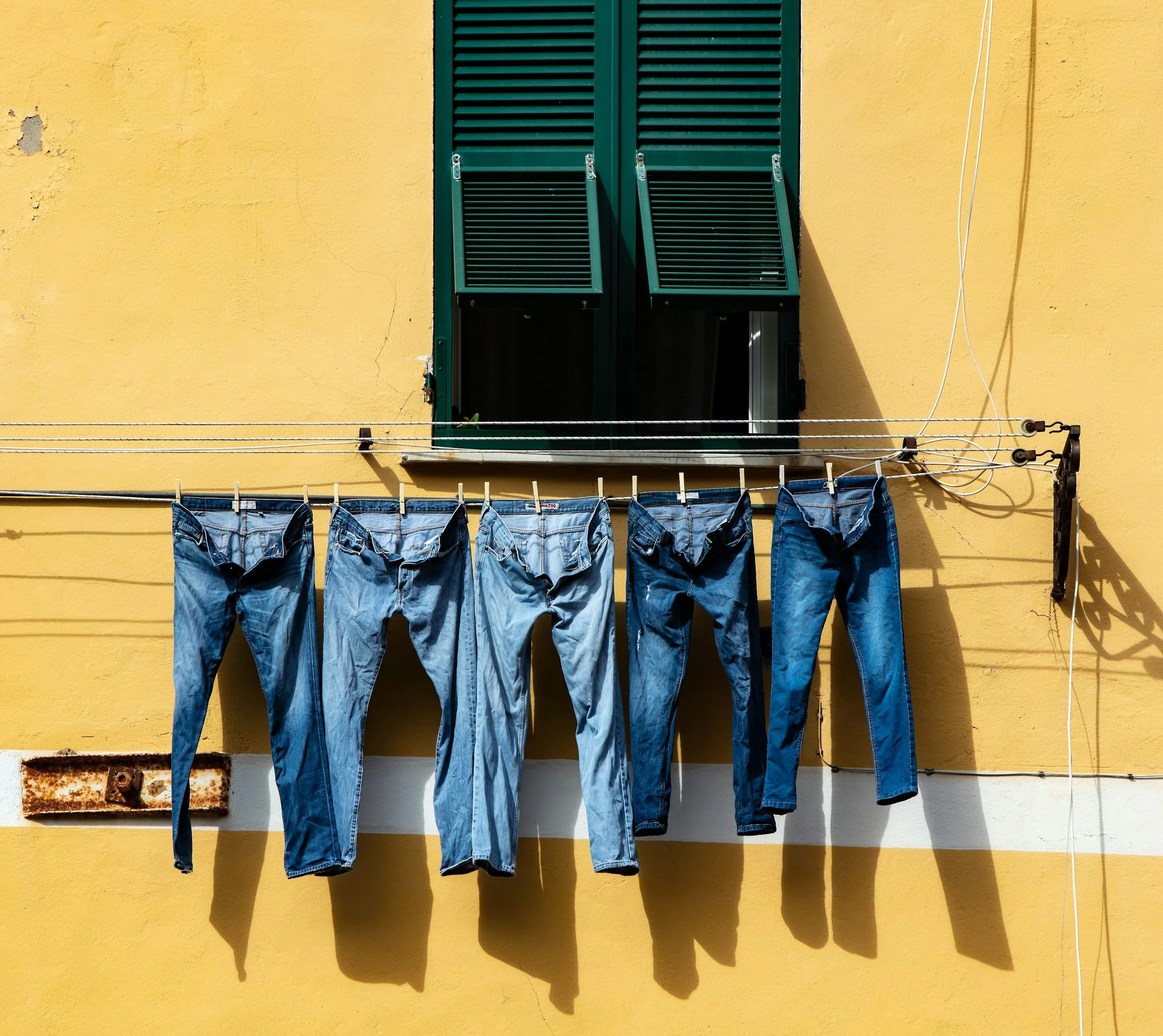 Yellow building wall with green window shutters, some laundry hanging on a clothesline, and electrical wiring.