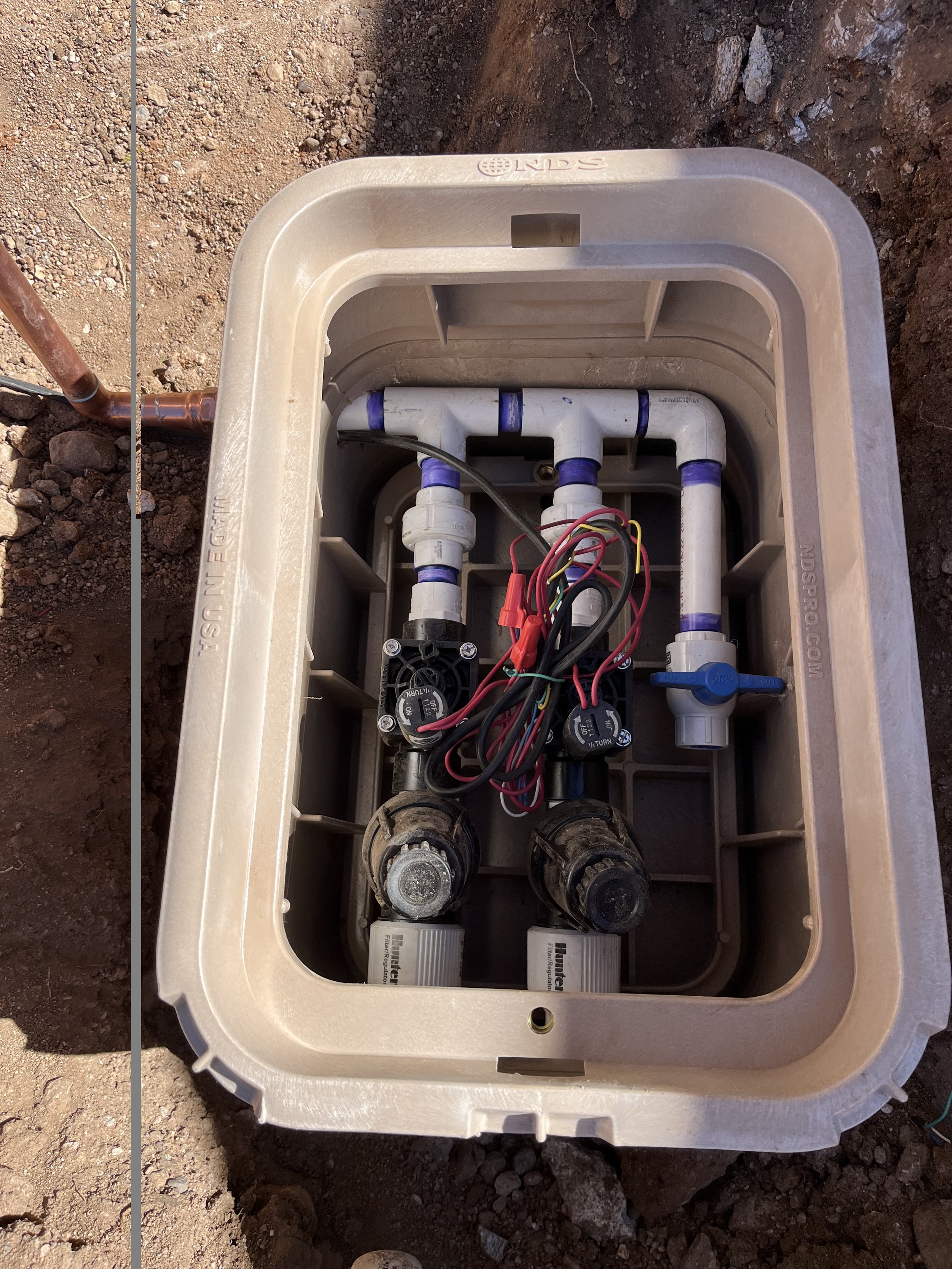 Electrical or plumbing electrical control panel or box with wires and valves inside, installed in a plastic enclosure on ground.