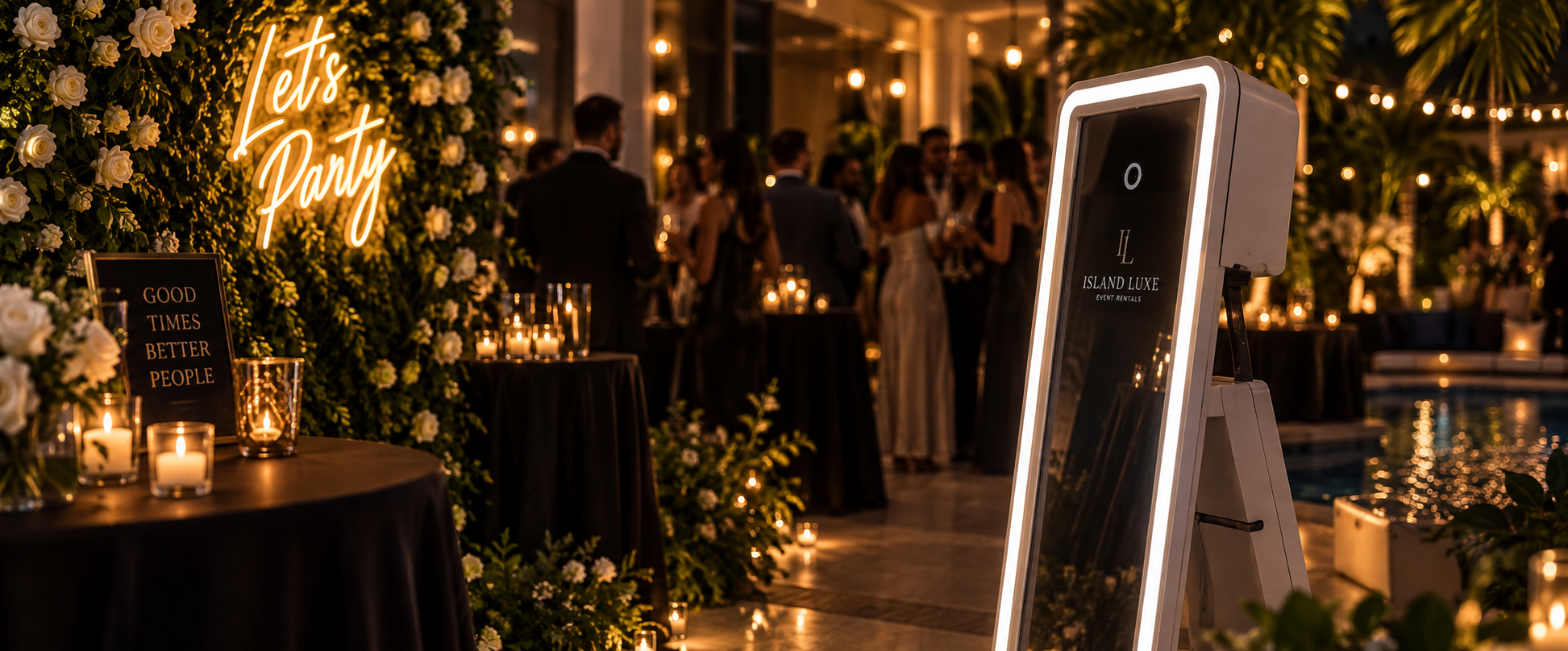 A floral wall with a neon sign that reads 'Let's Party,' and an interactive mirror photo booth from Island Luxe Event Rentals nearby.