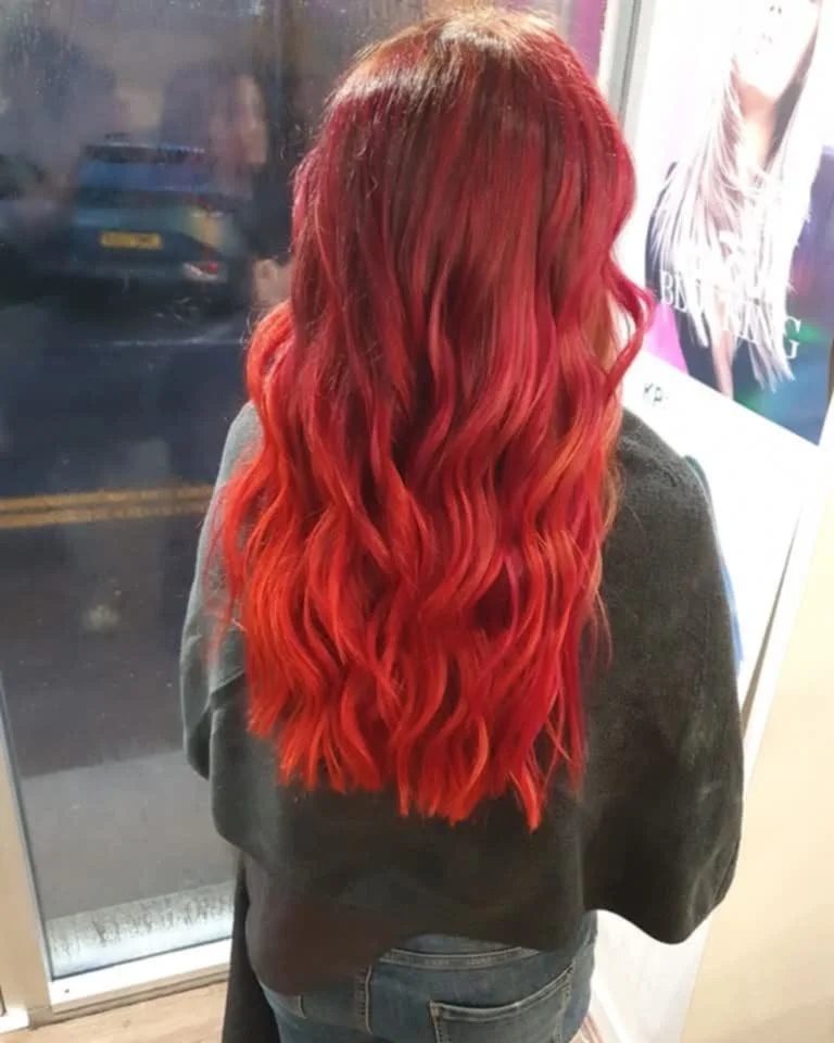 Woman with long, wavy red hair standing inside and looking out a window.