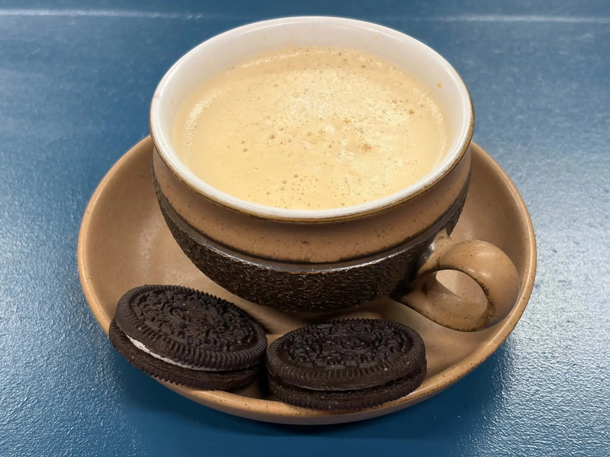 A cup of coffee or espresso on a saucer with Oreo cookies on a blue surface.