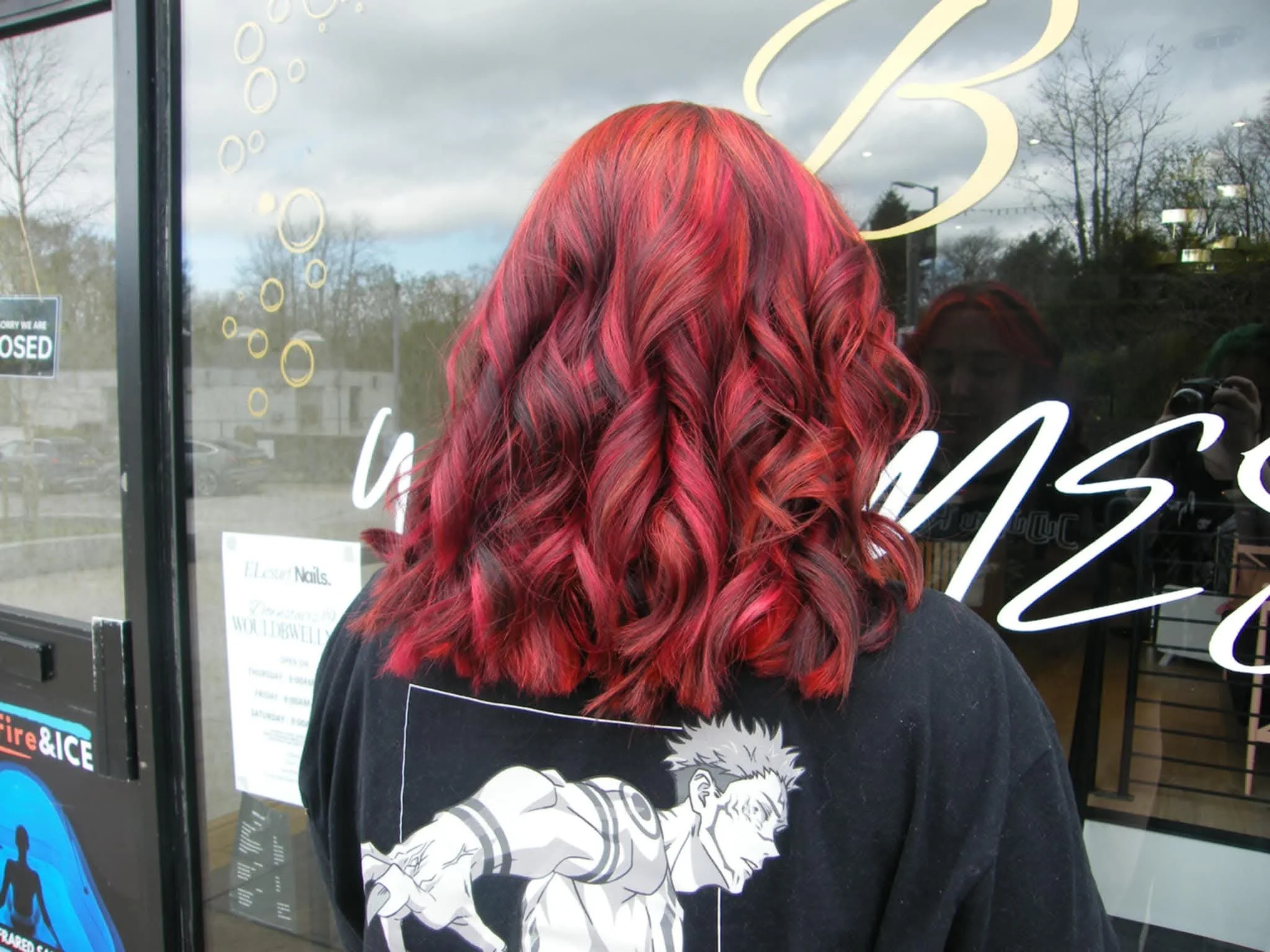 The back of a person with curly, long red hair standing in front of a glass door or window with neon signs.