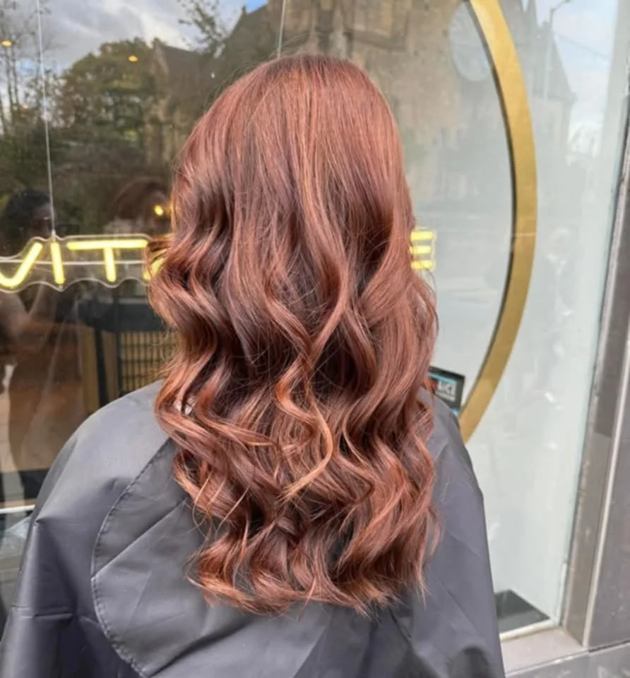 Back view of a woman with long, wavy, auburn hair.