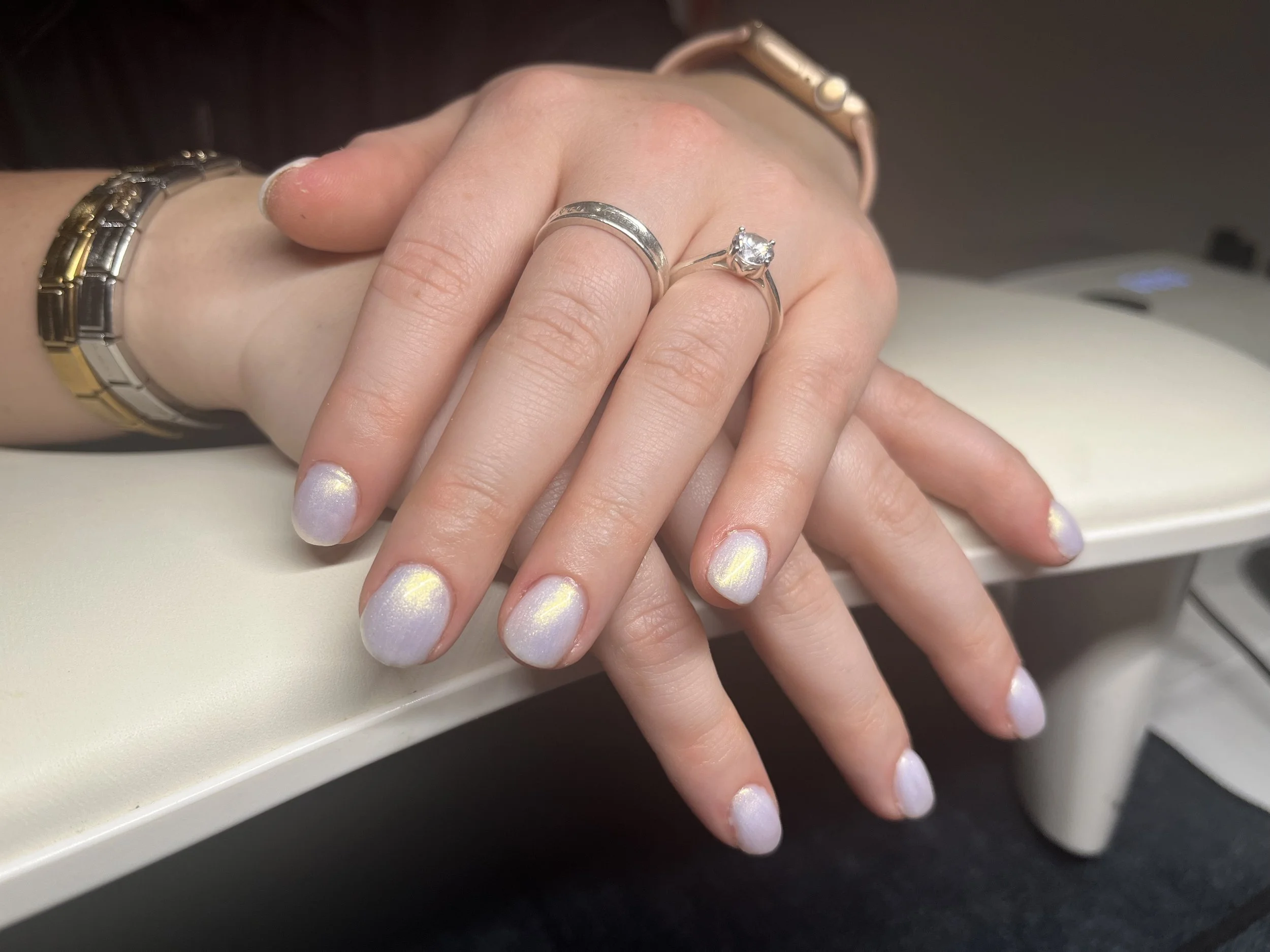 Close-up of a person's hand with manicured nails, wearing several rings, and a wristwatch, resting on a white surface.