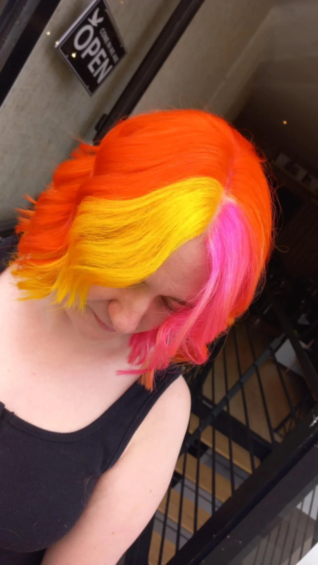 Woman with vibrant, multi-colored hair in shades of pink, yellow, orange, and red, styled in soft waves.