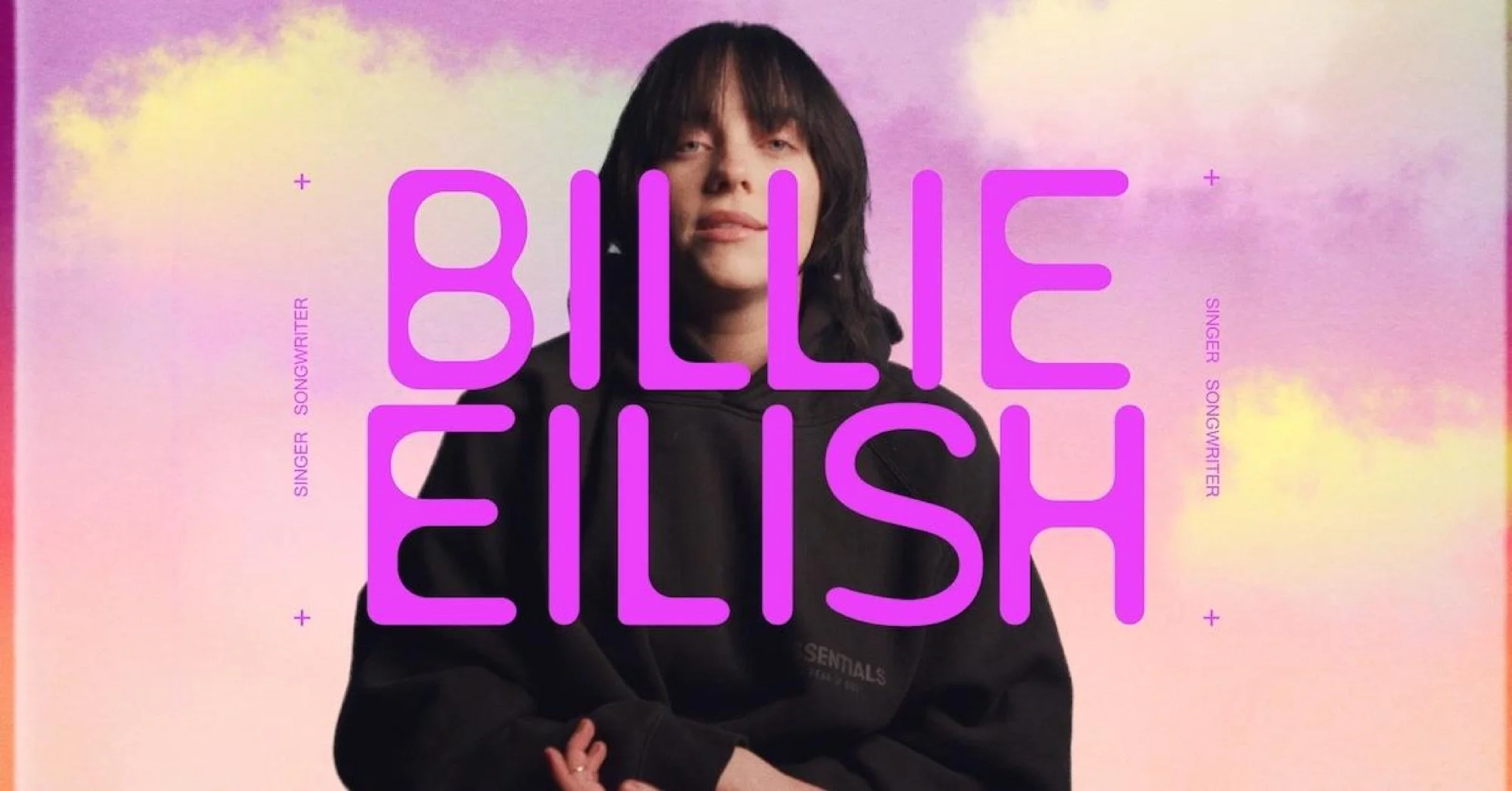 A woman with dark hair and a black hoodie posing against a pastel pink and purple sky background with yellow clouds. Large pink text reads 'BILLY EILISH'. Smaller vertical text on the left and right sides reads 'SINGER SONGWRITER'.