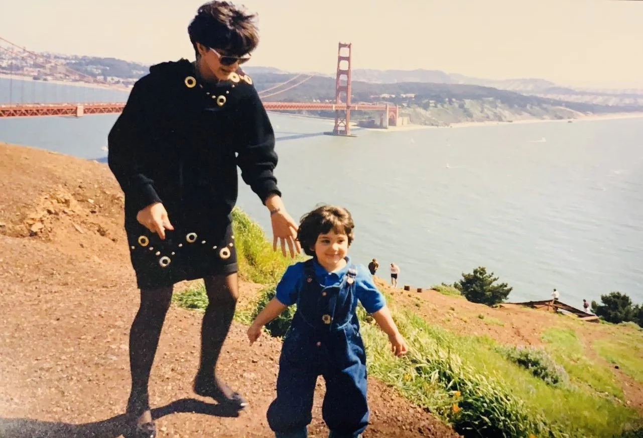 A woman and a young boy posing on a hill near the water with the Golden Gate Bridge in the background.