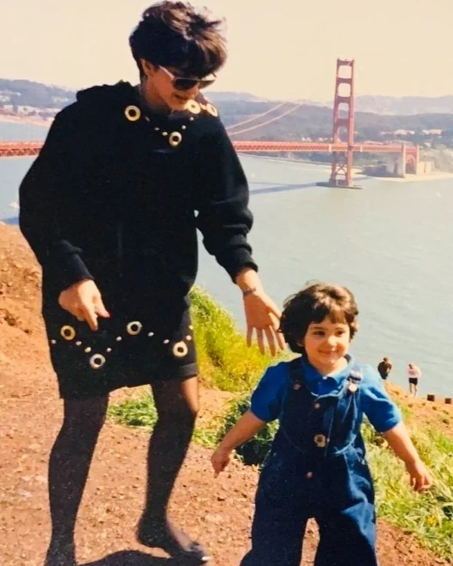 A woman and a young boy walking outdoors near water with the Golden Gate Bridge in the background.