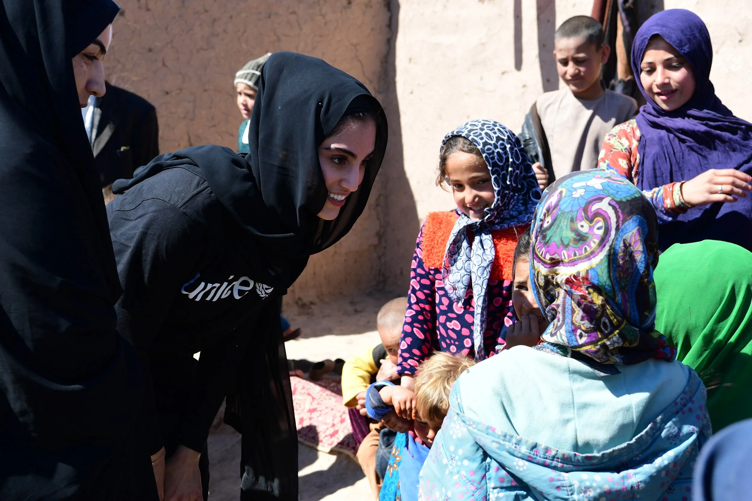 Women and children gathered outdoors, some wearing headscarves, engaging in a community activity or gathering.