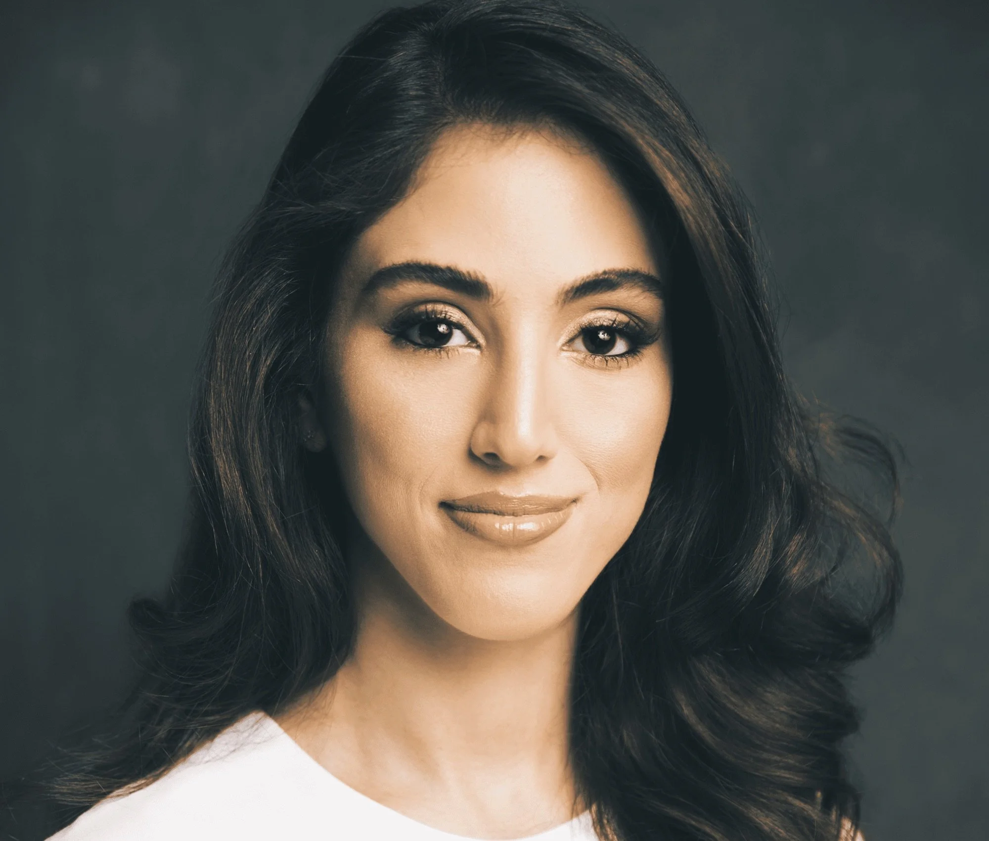 Close-up photo of a woman's face with long dark hair, well-groomed eyebrows, subtle eye makeup, and a soft smile, against a neutral background.
