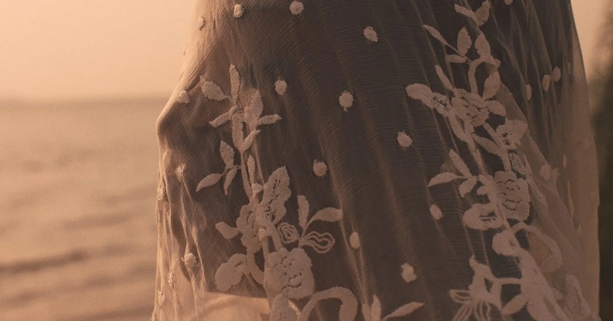 Close-up of a fabric with floral embroidery in white thread on a dark background.