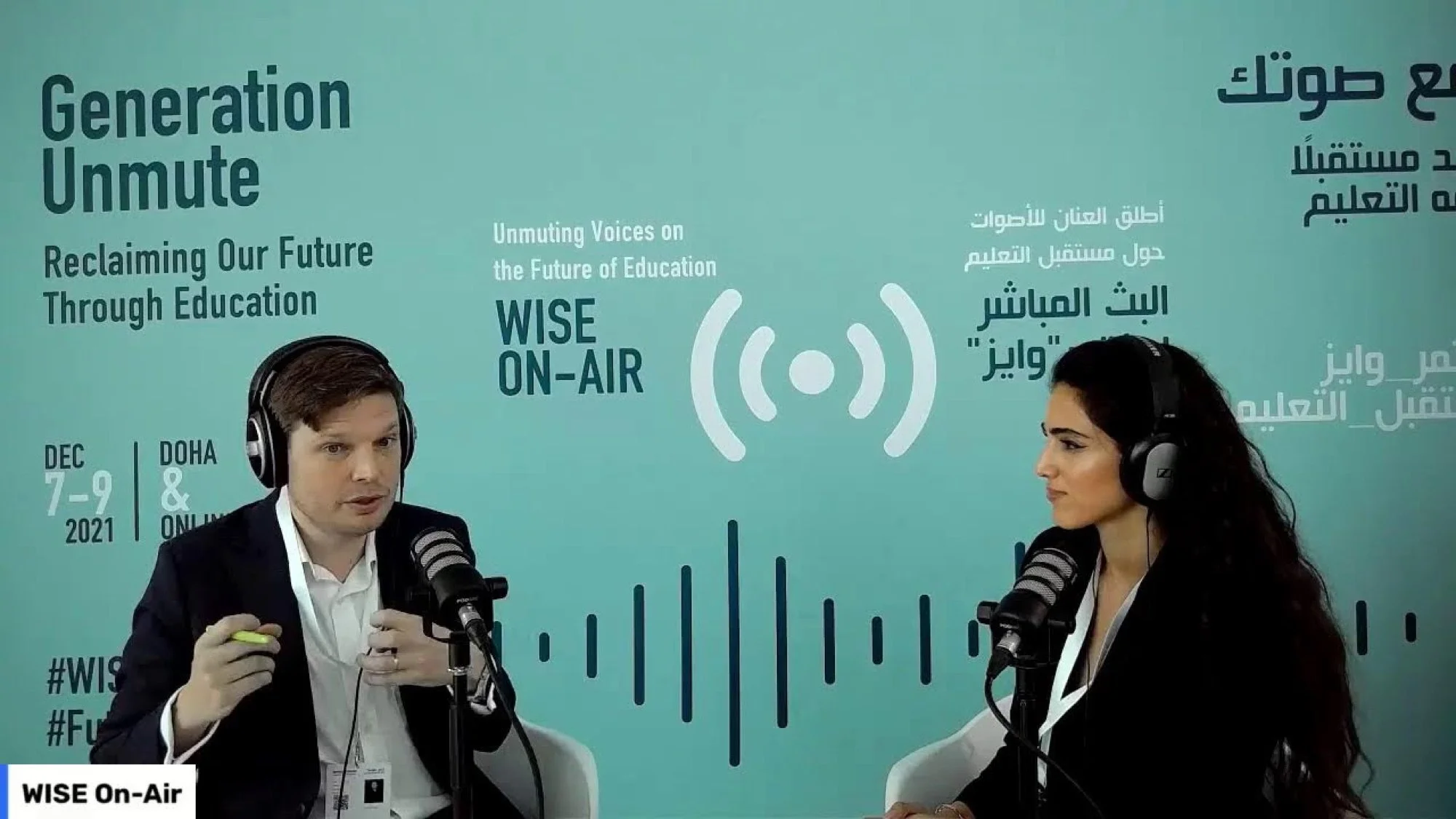 Two people, a man and a woman, are sitting at microphones wearing headphones, having a conversation during a live radio or podcast recording. They are in a studio with a teal background that displays the event name, date, and the phrase 'Unmute Voices on the Future of Education'.