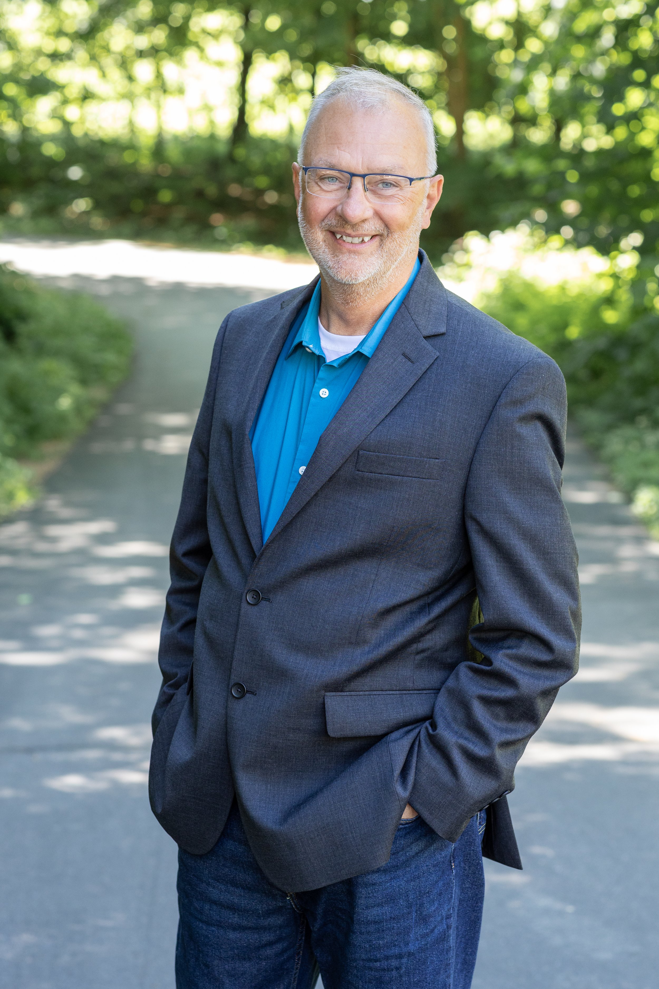 David Boisen, smiling, hands in pockets, standing in a wooded summer setting