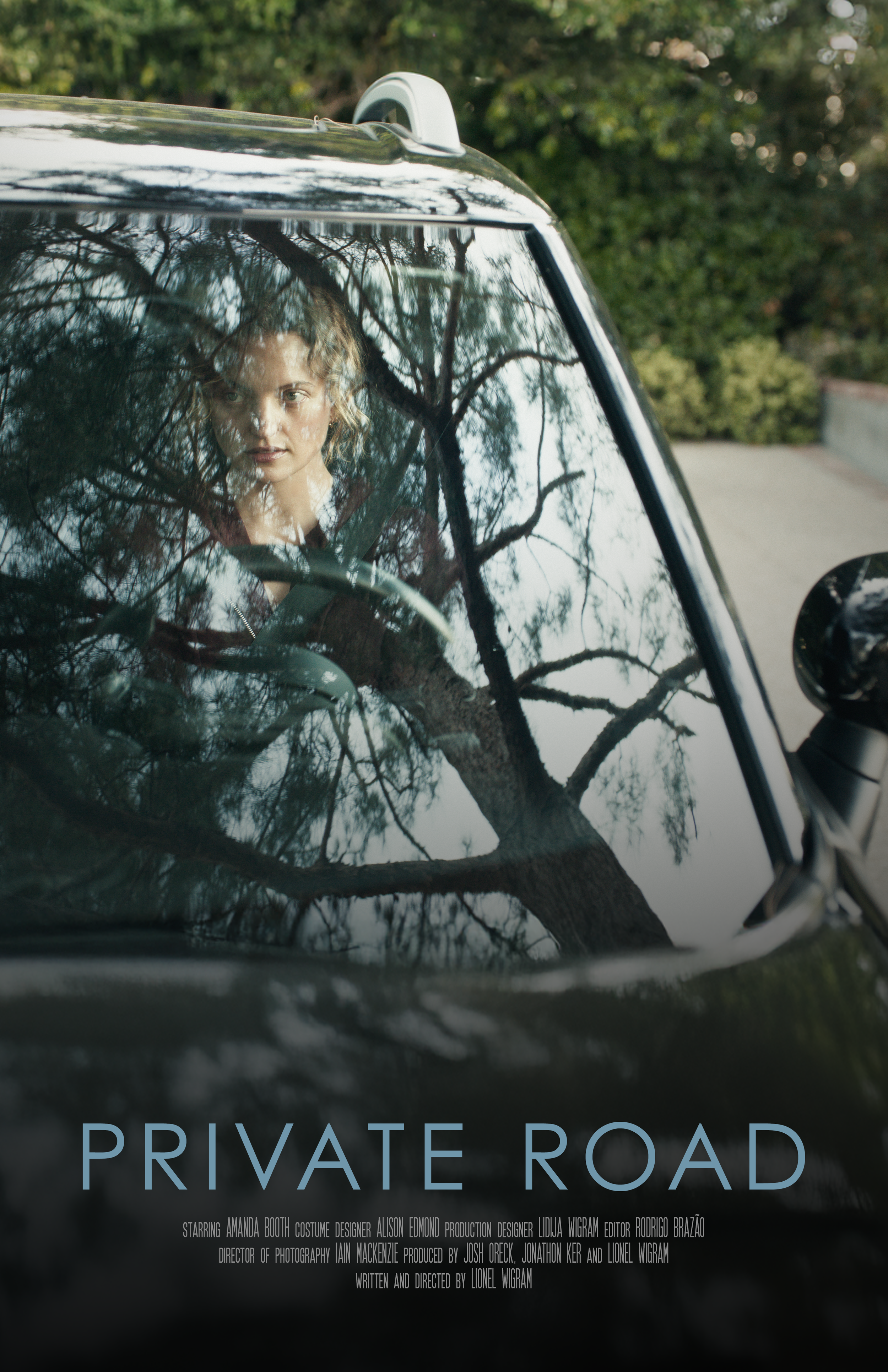 Close-up of a woman's face through a car windshield with tree branches reflected on the glass, and the words 'PRIVAT}E ROAD' on the bottom of the image.