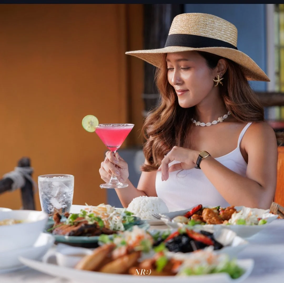 A pink cocktail with a lime garnish at a dining table with various dishes.