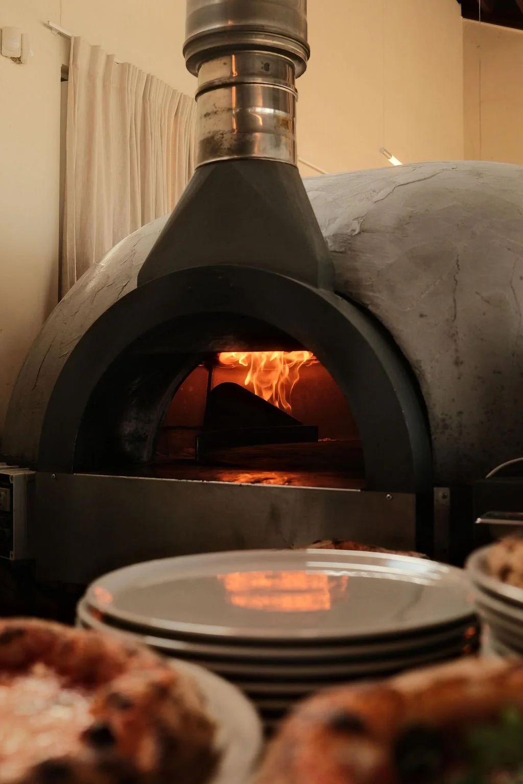 Horecafotografie van de houtgestookte pizzaoven bij Piatti Beach. Sfeervolle restaurant content door De Eetgency waarin vuur, verse pizza en de Italiaanse keuken samenkomen.