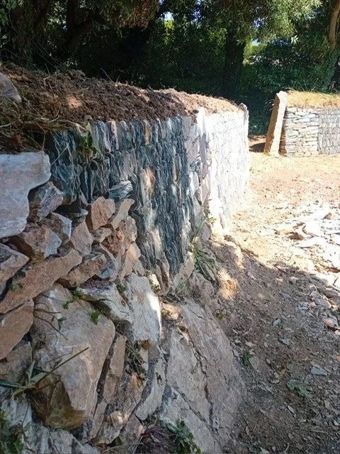 A stone and concrete retaining wall on a dirt path, with trees in the background.