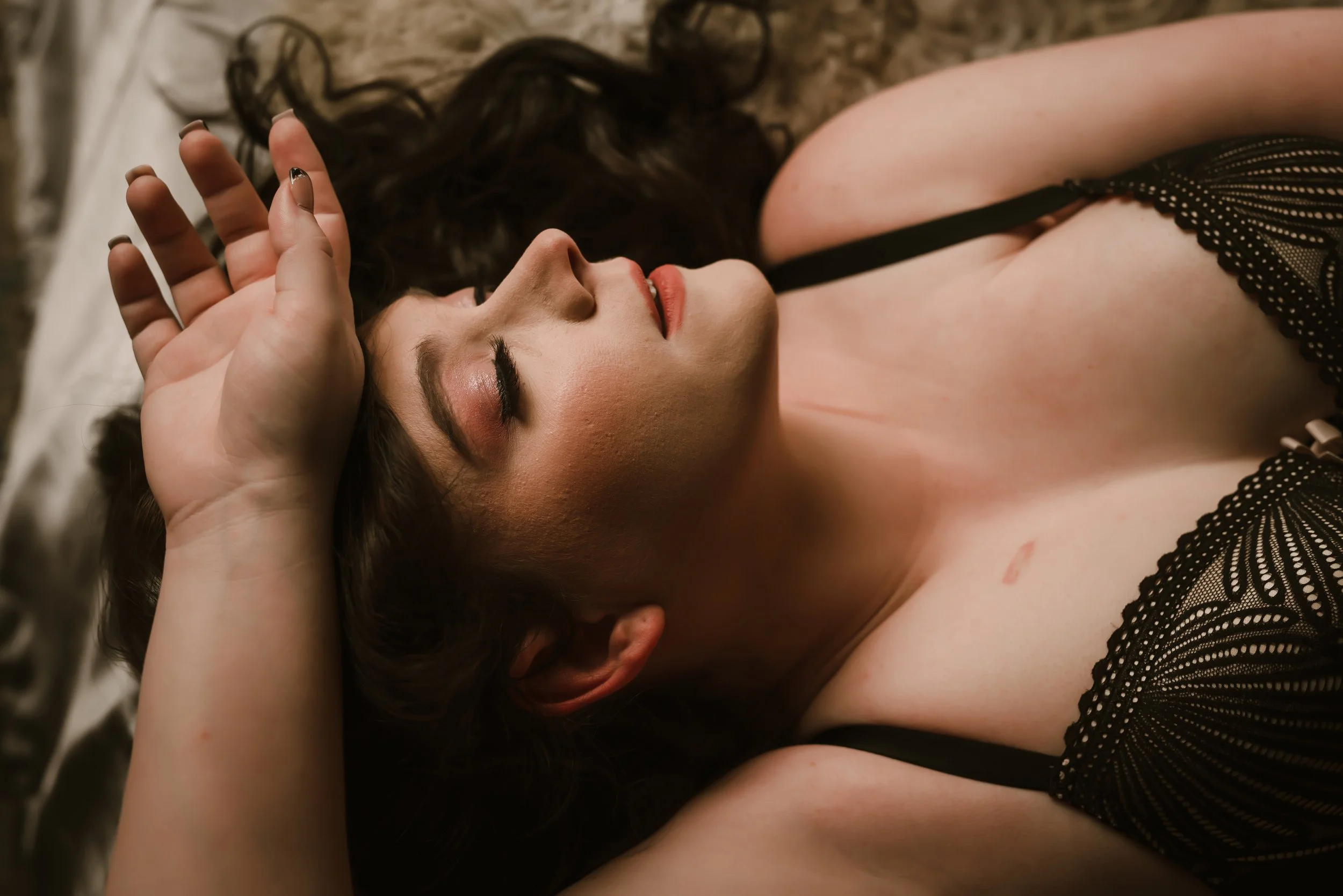 woman laying with hair covering head in black lace lingerie, while laying on bed