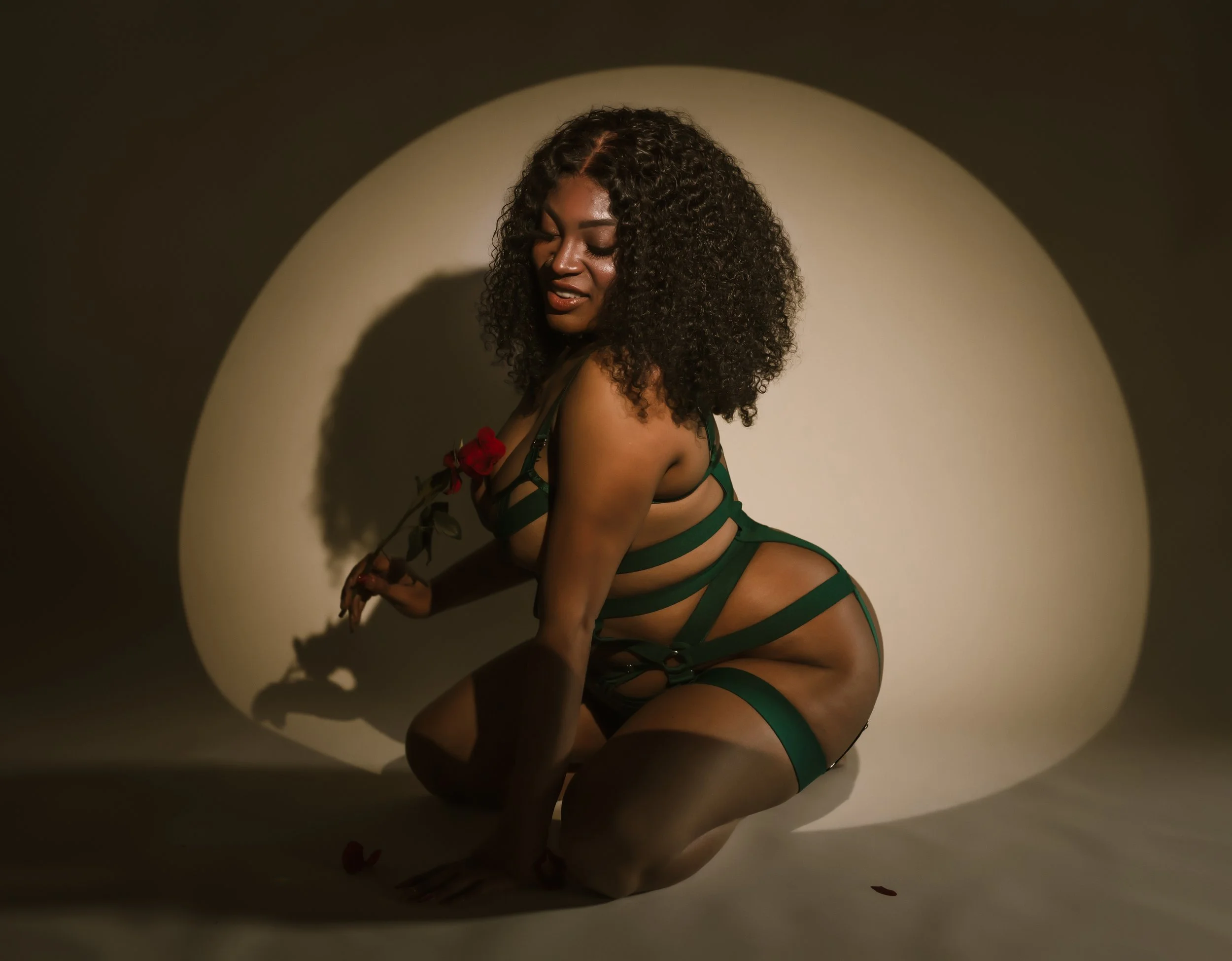 Woman in green lingerie holding a red rose in front of a circular light source creating a halo effect.