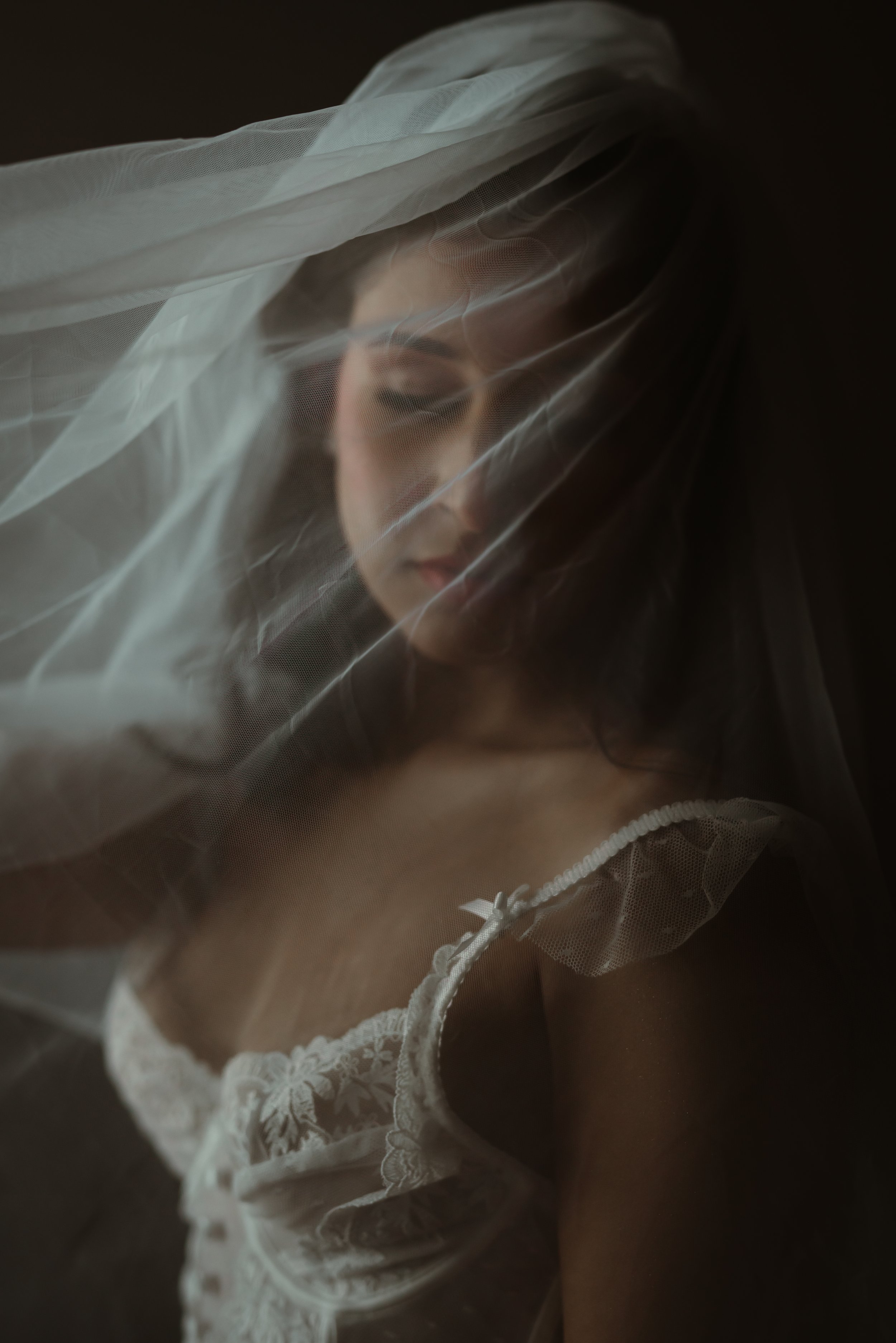 A woman with a veil covering her face, dressed in white lace lingerie with white lace details.