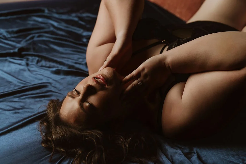 A woman lying on a bed, wearing black lingerie, with her eyes closed and hands near her face.