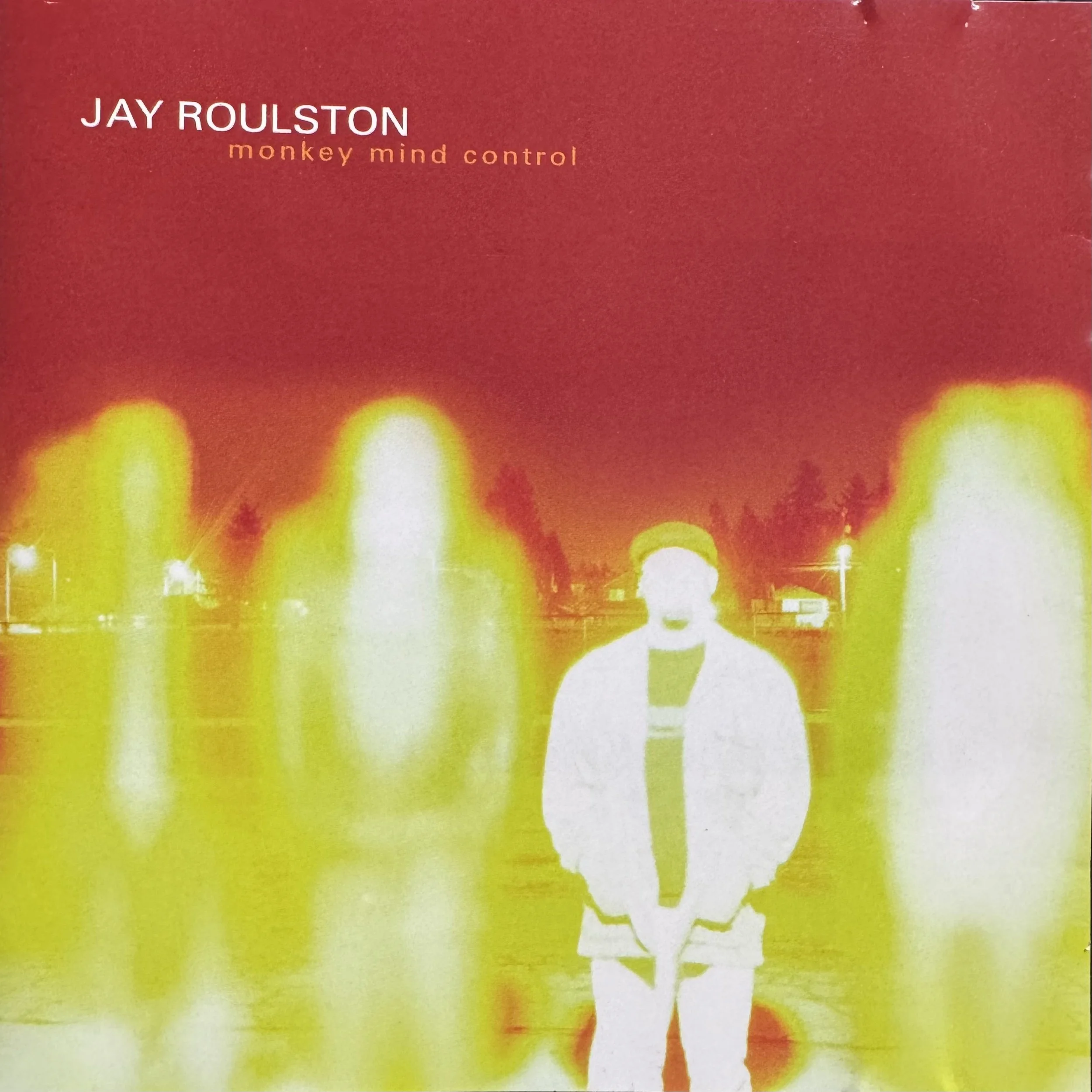 Close-up of a book cover with a red background, featuring the text 'JAY ROULSTON' and 'monkey mind control' in white and orange fonts respectively, with blurred yellow and red lights at the bottom.