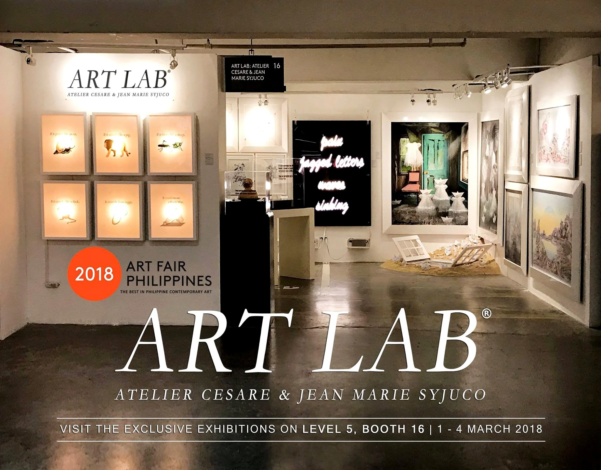 Photo of an art gallery exhibit featuring artworks with text and images, including a black sign with white text and framed art pieces on white walls.