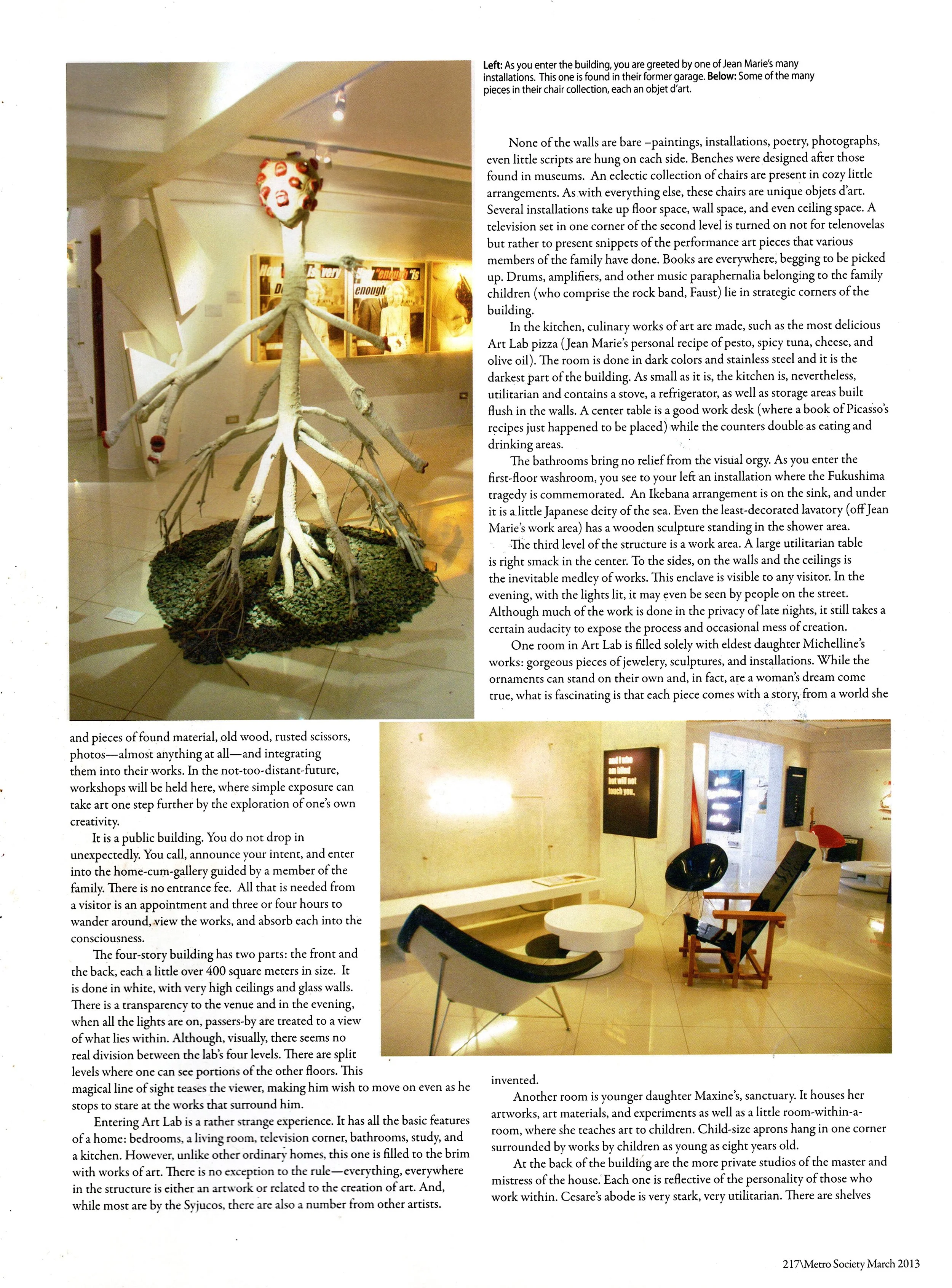 Photo of contemporary art gallery interior showcasing sculptures, installations, and artistic pieces. Prominent sculpture resembles a multi-armed octopus with a face, situated on a circular gravel base. The gallery has white walls, warm lighting, and