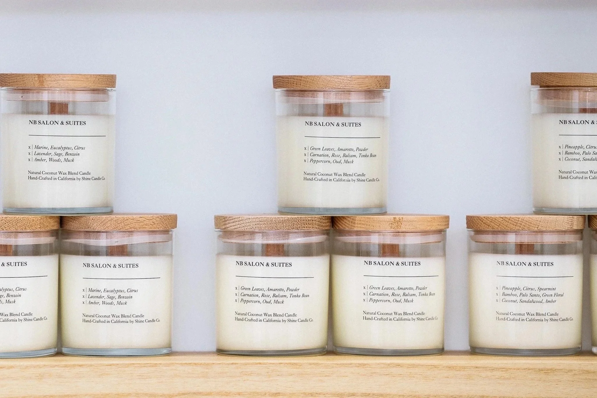 Multiple candles in glass containers with wooden lids labeled 'NB SALON & SUITES' and various scent descriptions. Candles non toxic , locally handmade. natural ingredients, top candles in Newport Beach, top candles in corona Del Mar