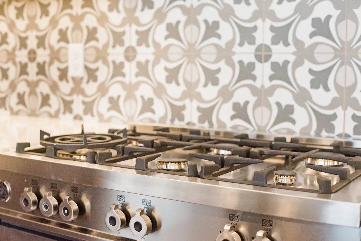 A stainless steel gas stove with four burners and control knobs, set against a patterned tile backsplash.