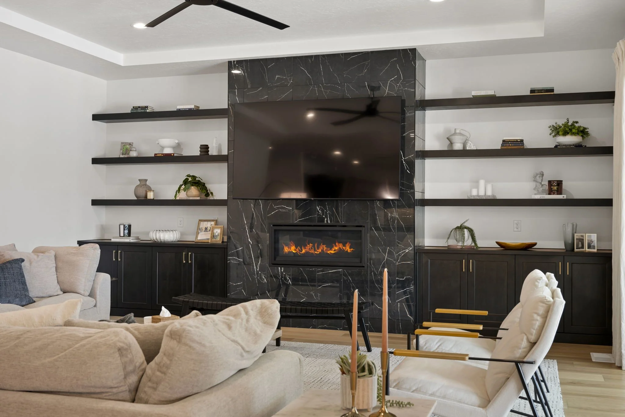 Living room with a black marble fireplace, wall-mounted TV, and open black shelves with decorative items, plants, and books.