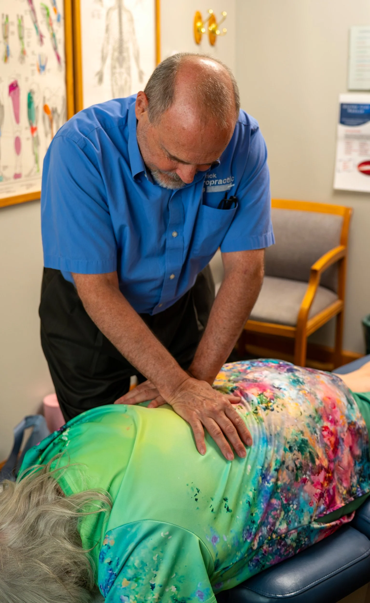 A chiropractor performing an adjustment on a patient lying face down on a treatment table in a medical office.