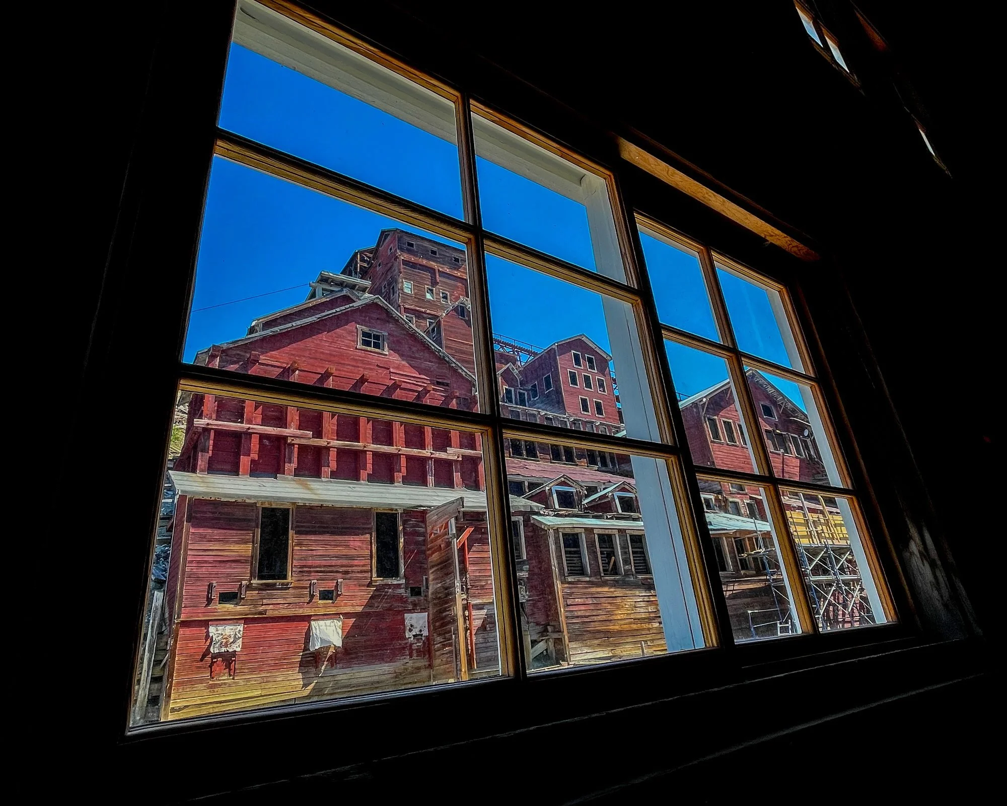 Looking up through a window at a bright blue sky and a red cabin that is under construction, with scaffolding around it.