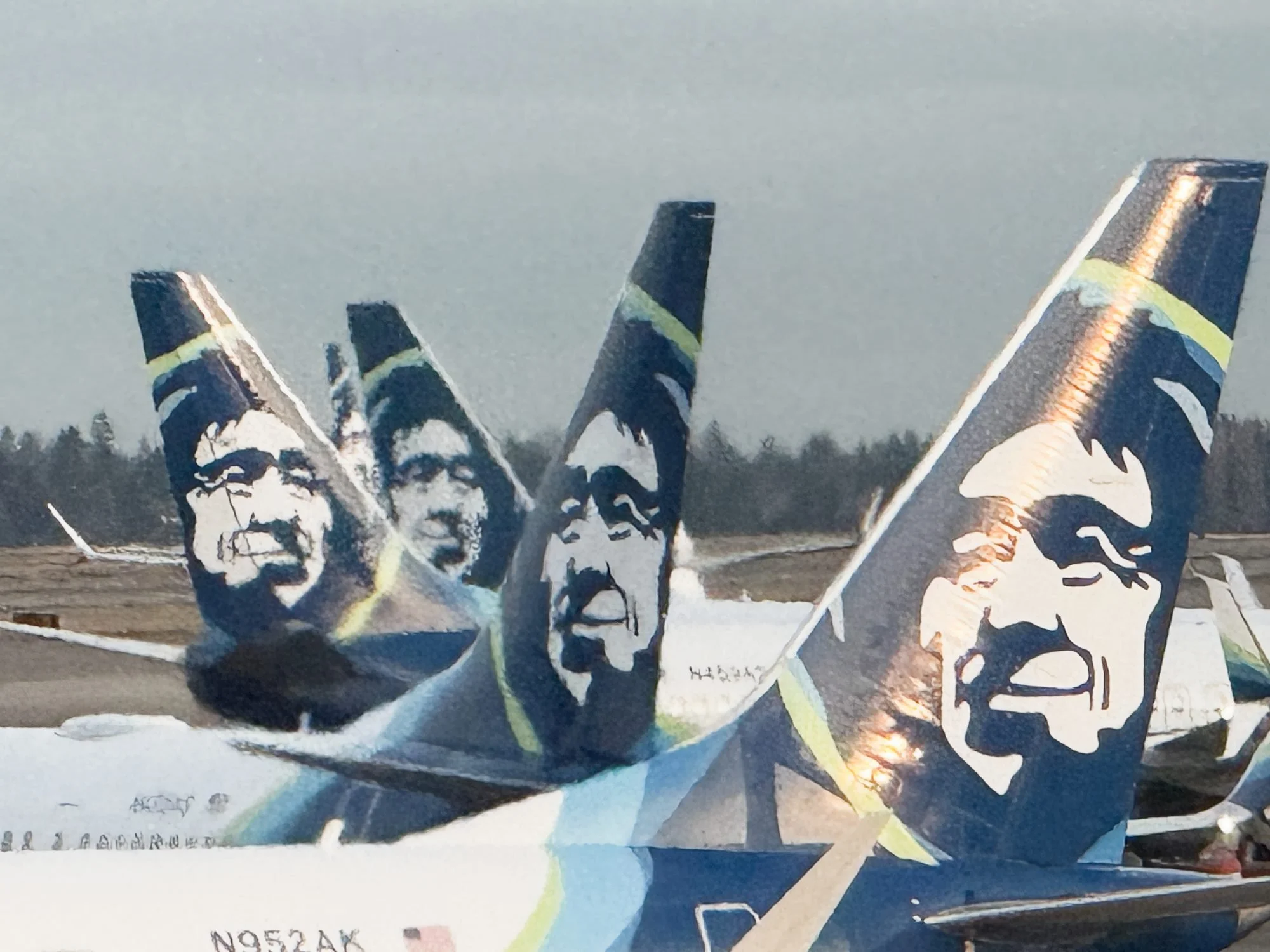 An art piece featuring black and white portraits of multiple individuals, painted on what appears to be a newspaper or billboard material. The portraits include both men and women, with some faces displaying serious expressions.