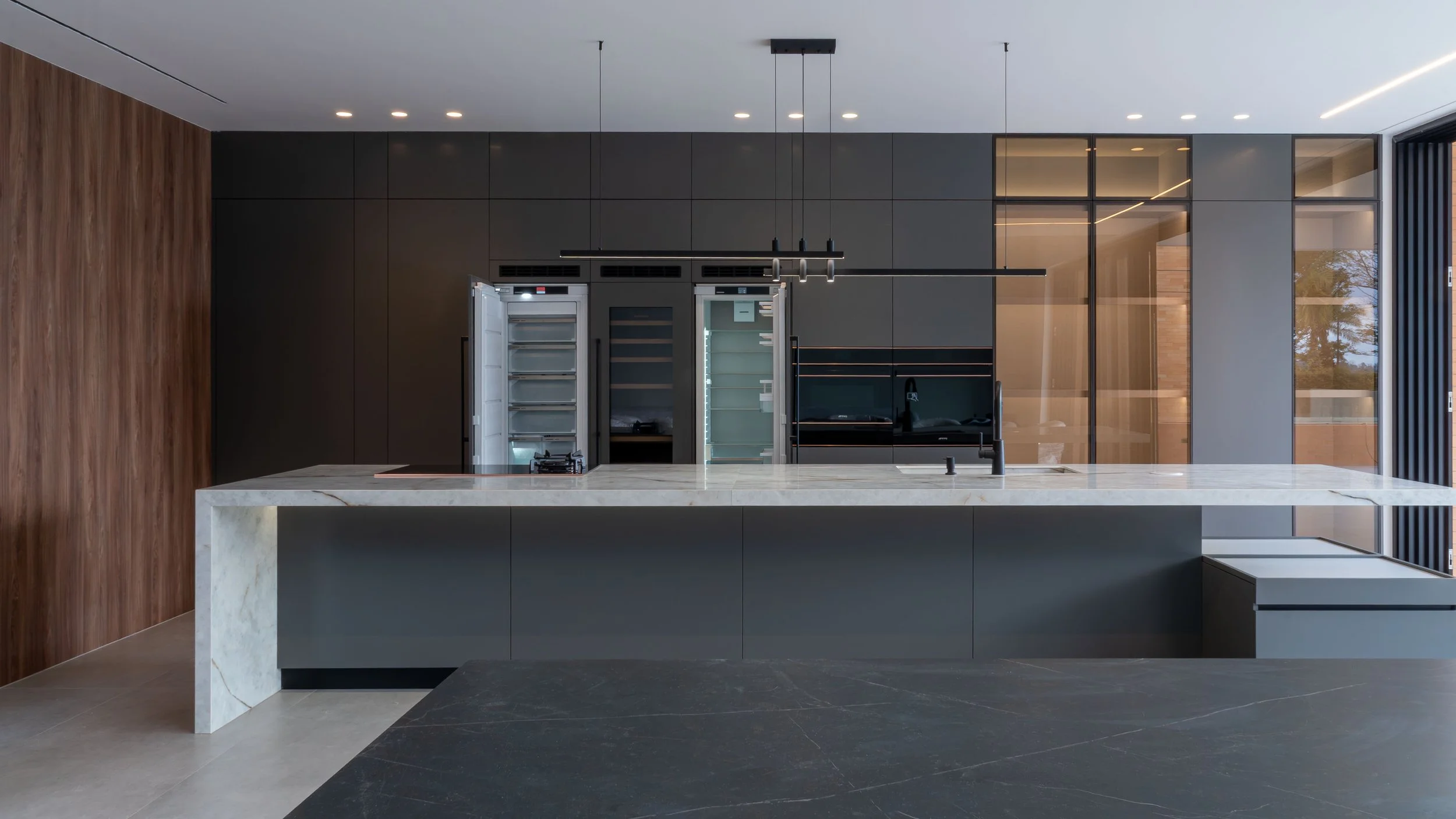 Cocina moderna con encimera de piedra sinterizada, carpintería arquitectónica en tonos grisesy paredes de vidrio con vista a un patio interior.