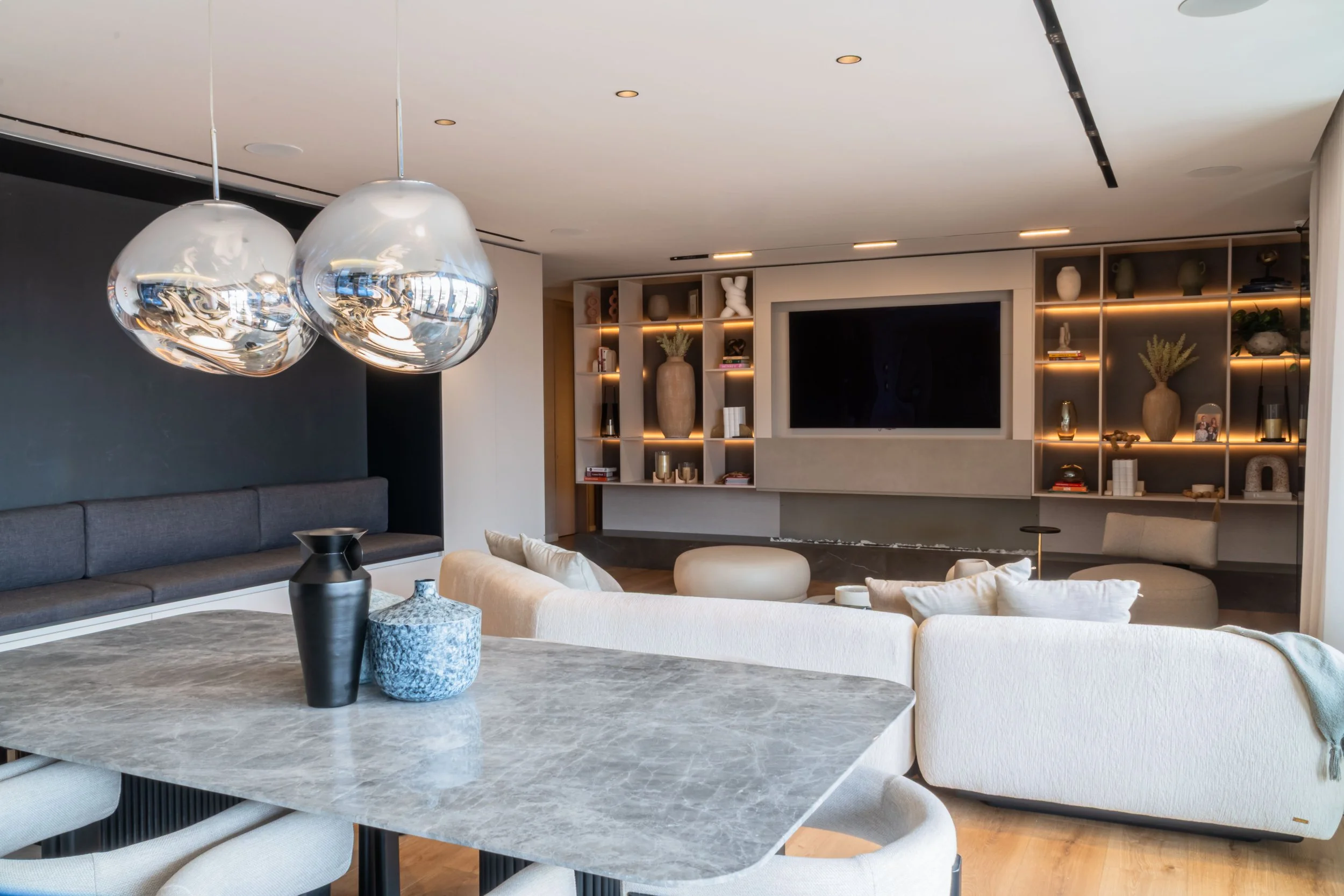 Sala moderna con lámparas del artista tom Dickson, mesa de piedra sinterizada , sillones blancos y estanterías con decoraciones y un televisor grande