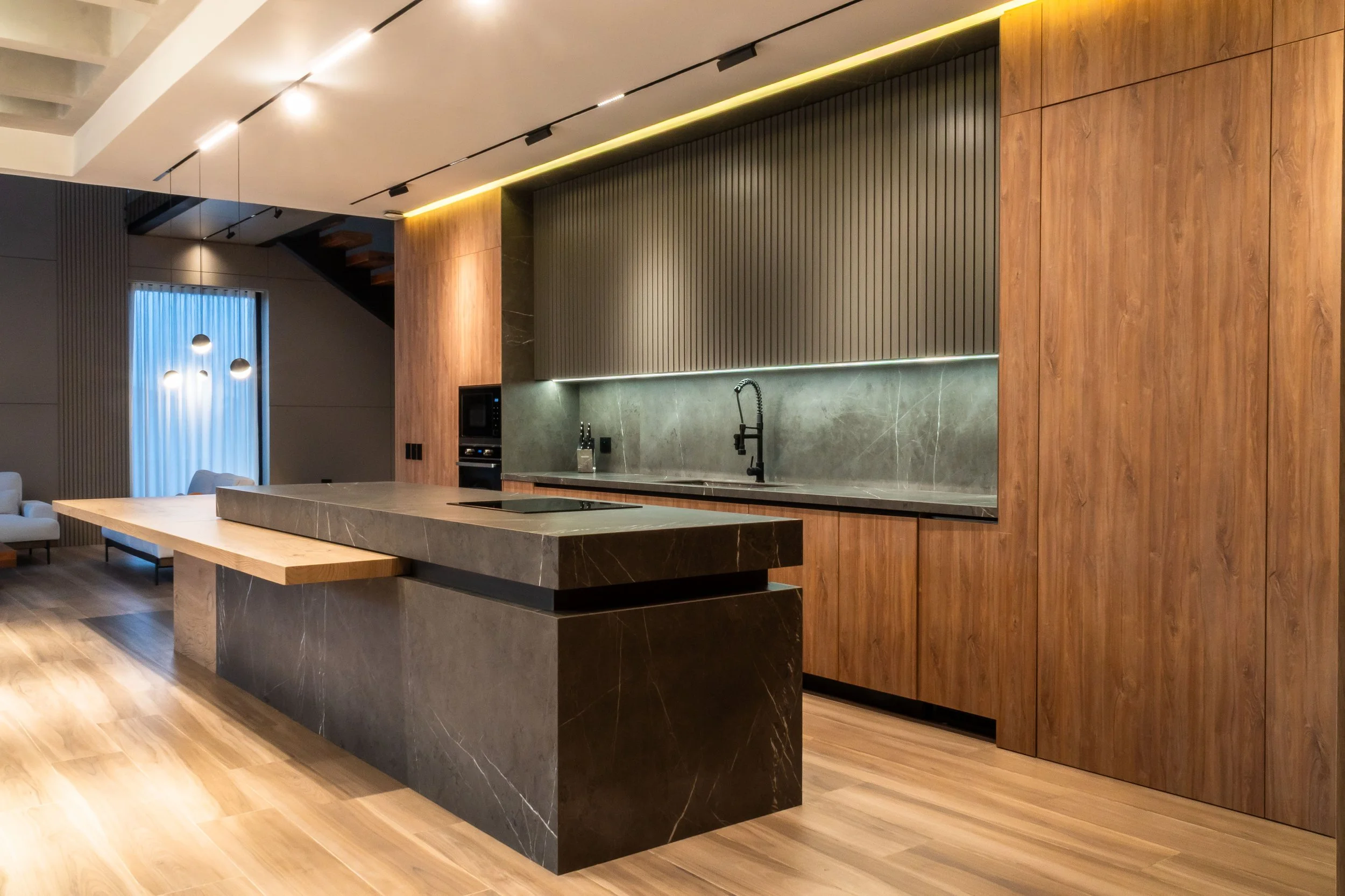 Interior moderno de cocina con encimera de piedra sinterizada, paredes de madera y grifería negra, iluminación indirecta